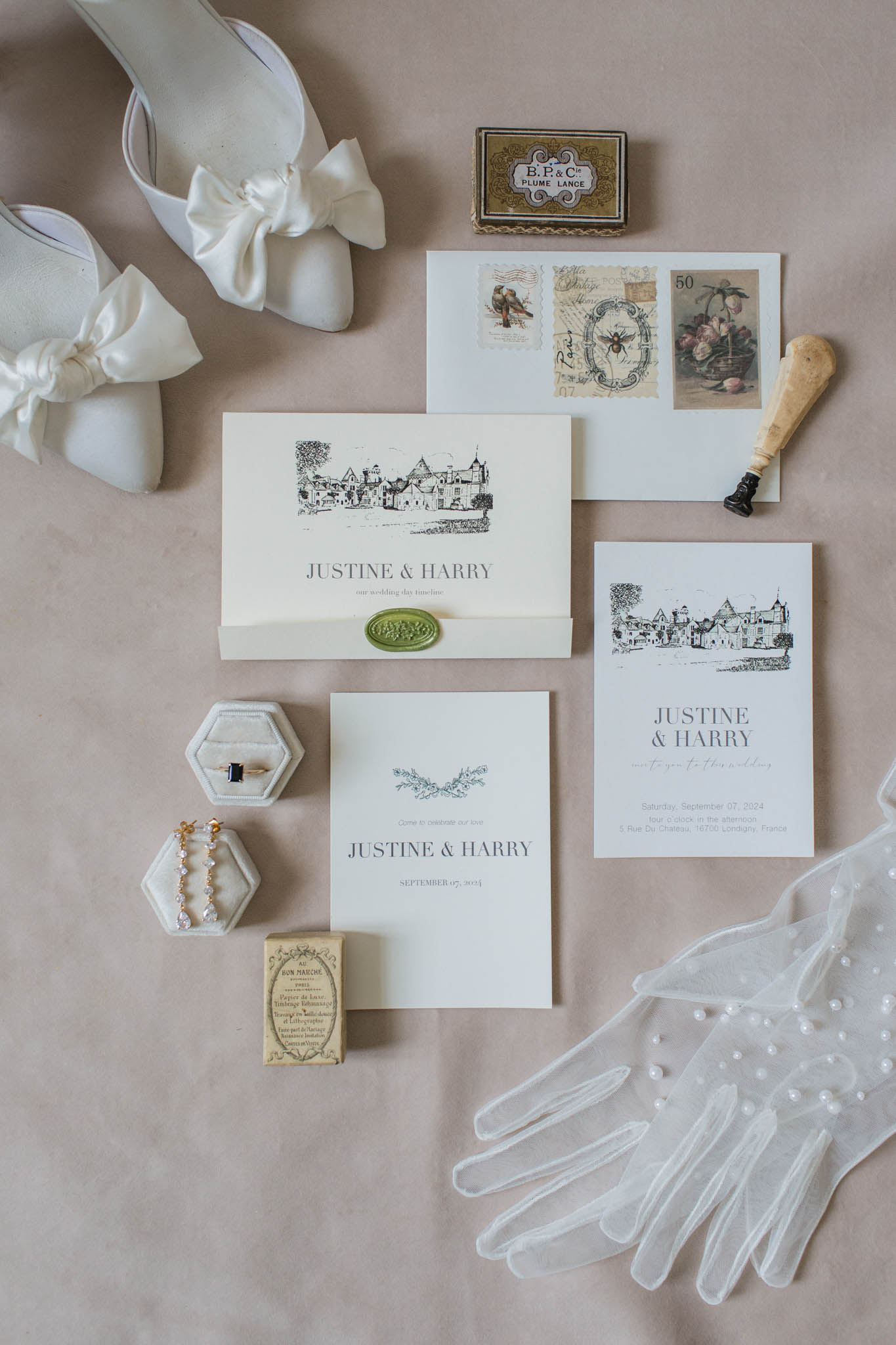 Flat lay of chateau-illustrated invite with sage wax seal, ivory shoes, pearl veil, gold ring dishes and stamps