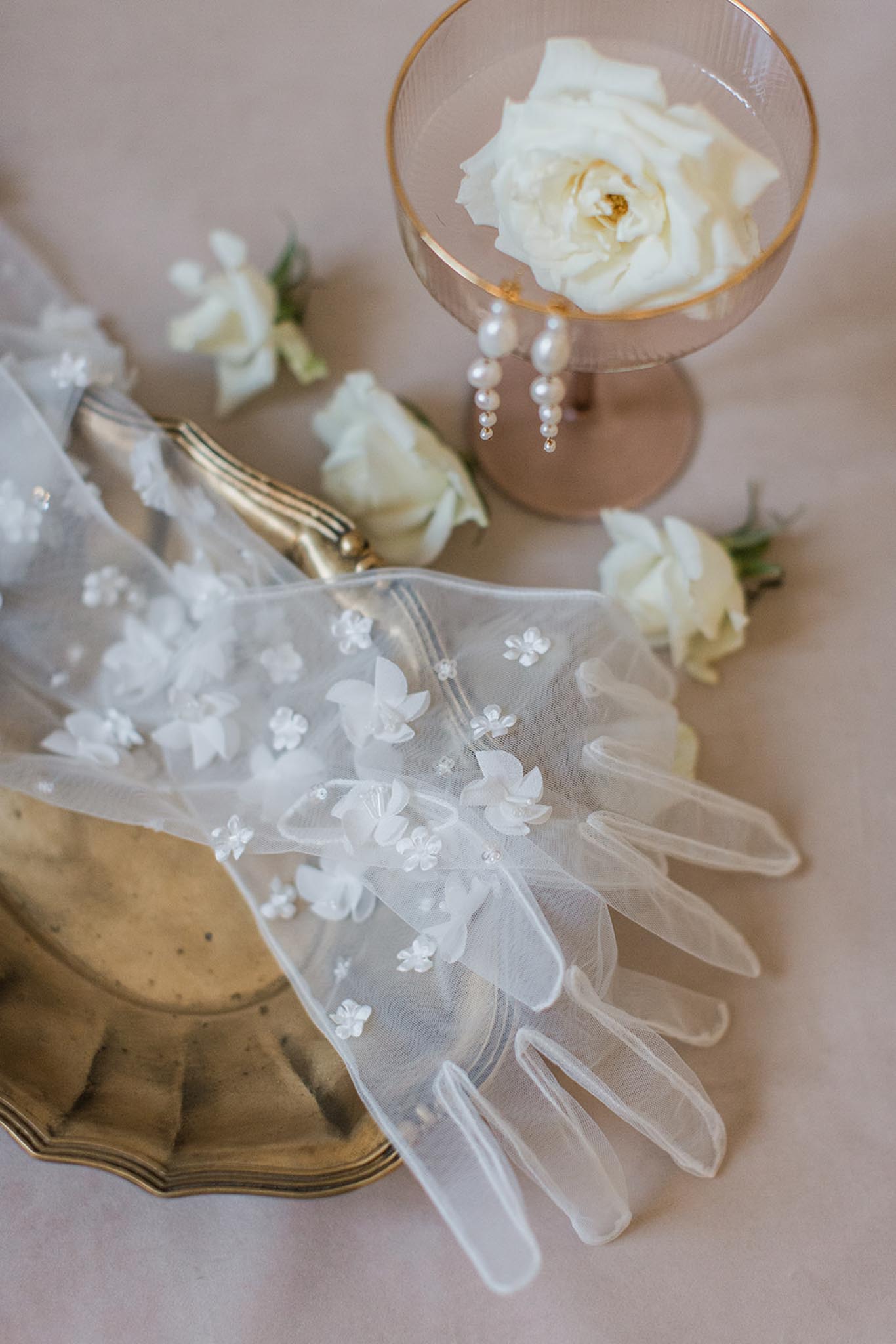 Flat lay of embellished veil with floral appliques, ivory roses, pearl earrings, and gold-rimmed charger