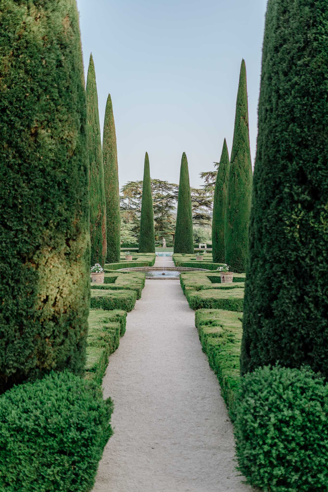 Symmetrical formal garden allee with Italian cypress trees, manicured hedges and central reflecting pool