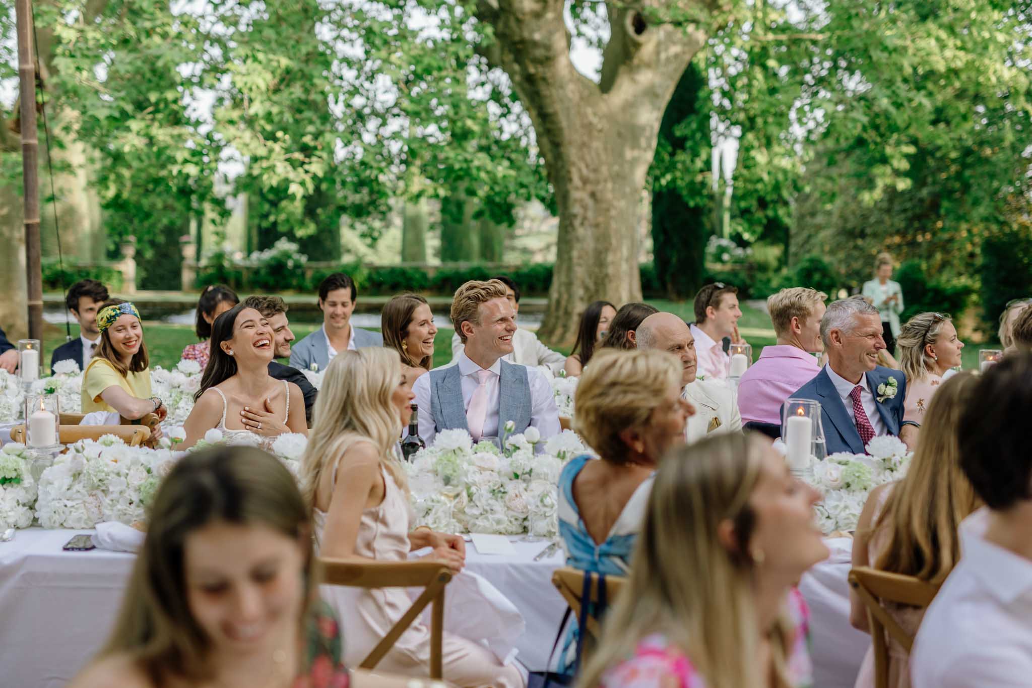 Outdoor garden reception with guests seated at long tables beneath blossoming trees at Chateau de Sannes