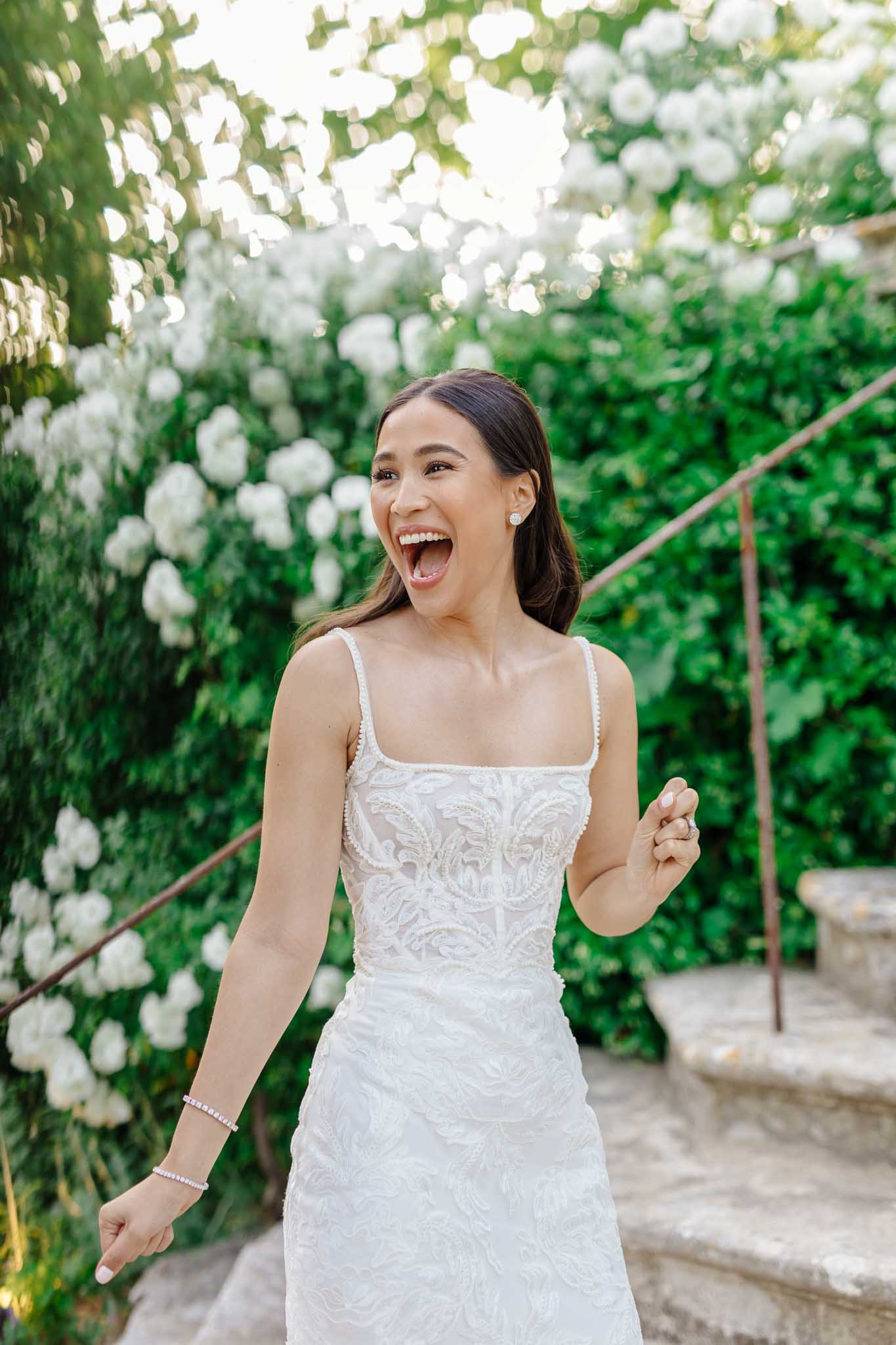 Laughing bride in beaded white dress framed by ivy walls and white flowering vines in a garden archway