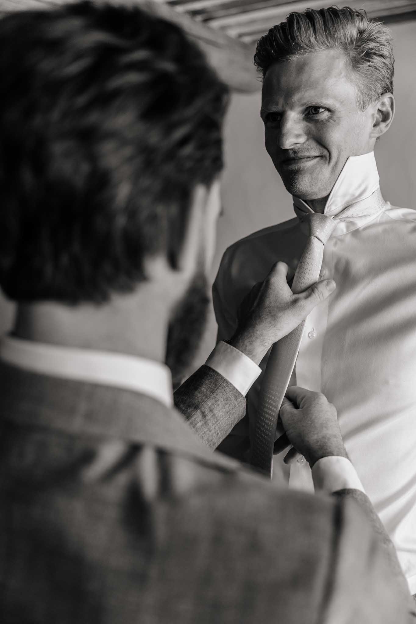 Black-and-white close-up of groom adjusting necktie during getting-ready preparations