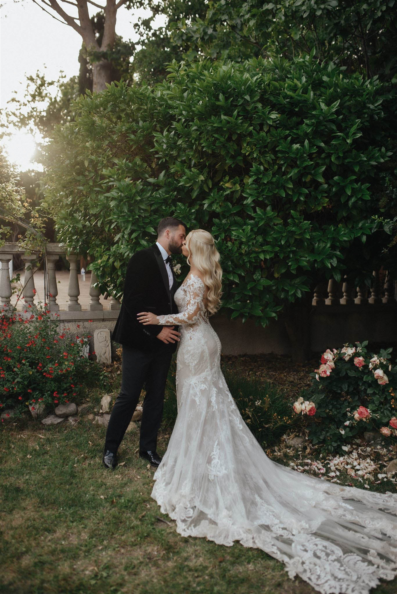 Couple kissing at golden hour bride in long-sleeve lace gown with cathedral train spread across foreground