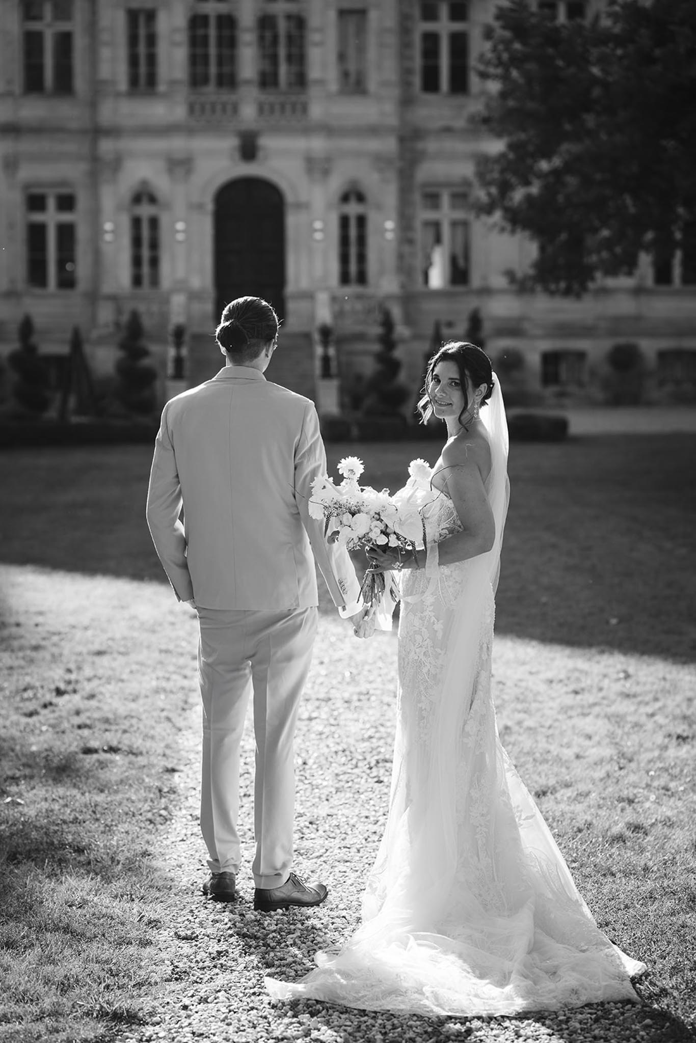 Black-and-white couple portrait on gravel courtyard before symmetrical classical stone manor with topiary