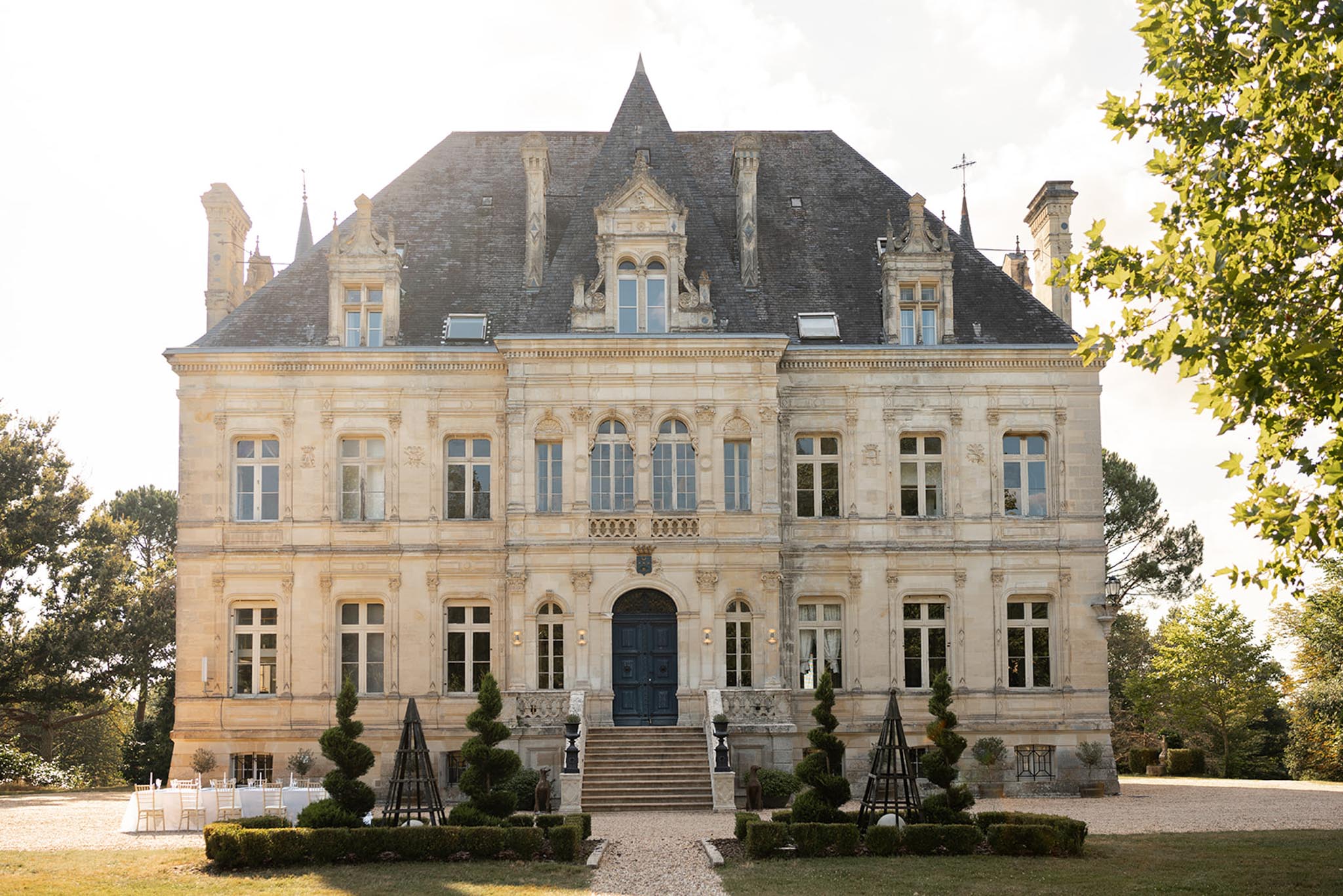 19th-century limestone château with mansard roof and white Chiavari chairs arranged on gravel courtyard for ceremony