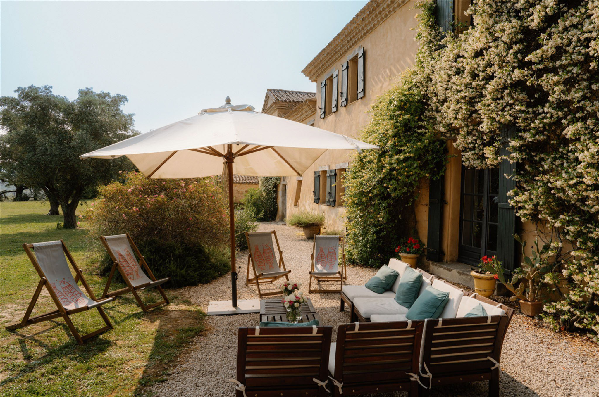 Provencal mas terrace with parasol, deck chairs, and lounge seating against ochre facade with climbing white vines