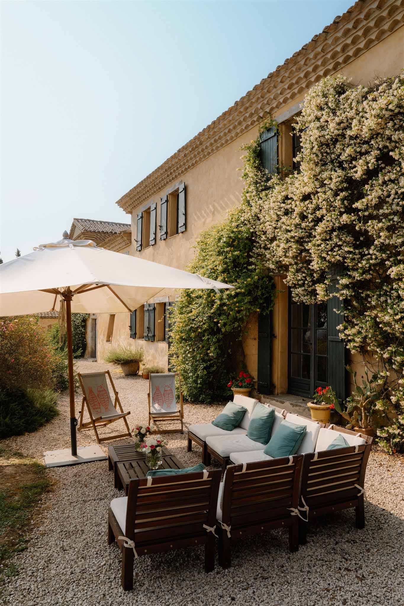 Provencal mas exterior with ochre walls, grey-green shutters, and outdoor lounge seating on gravel courtyard