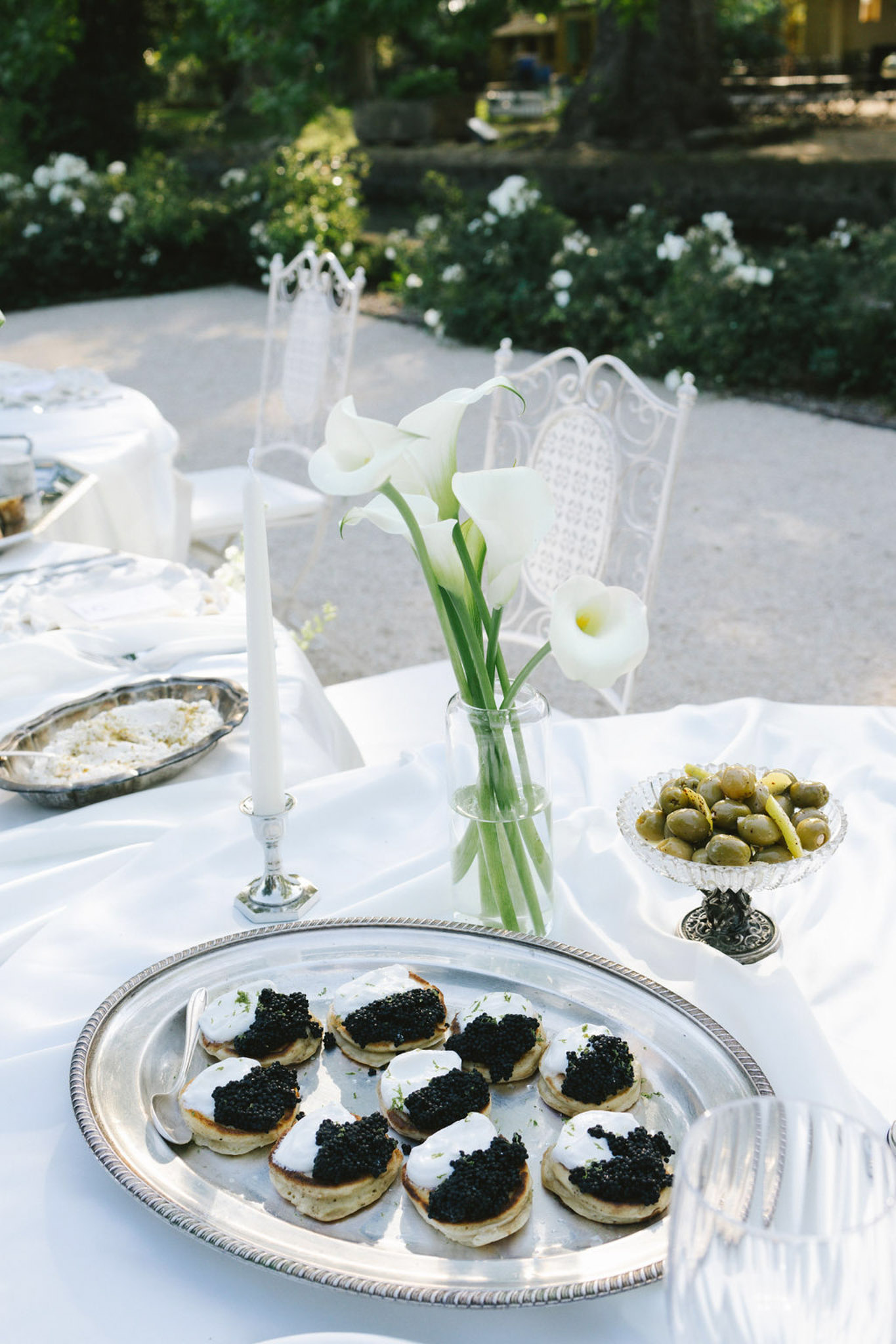 Outdoor reception table with caviar canapes, calla lily centerpiece, silver candlesticks and white chiavari chairs