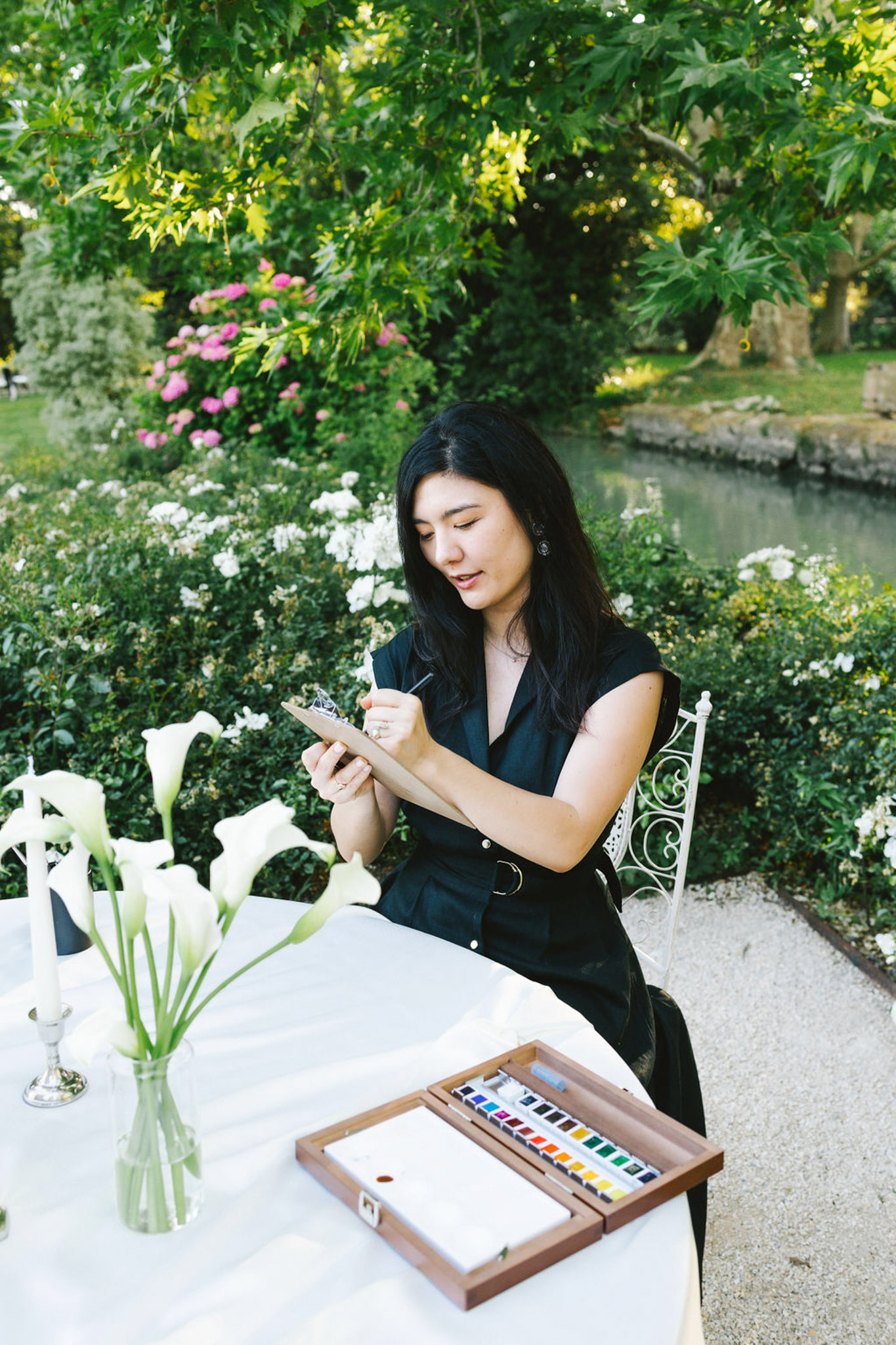 Live painter working at white-draped table with calla lilies in lush garden during wedding reception