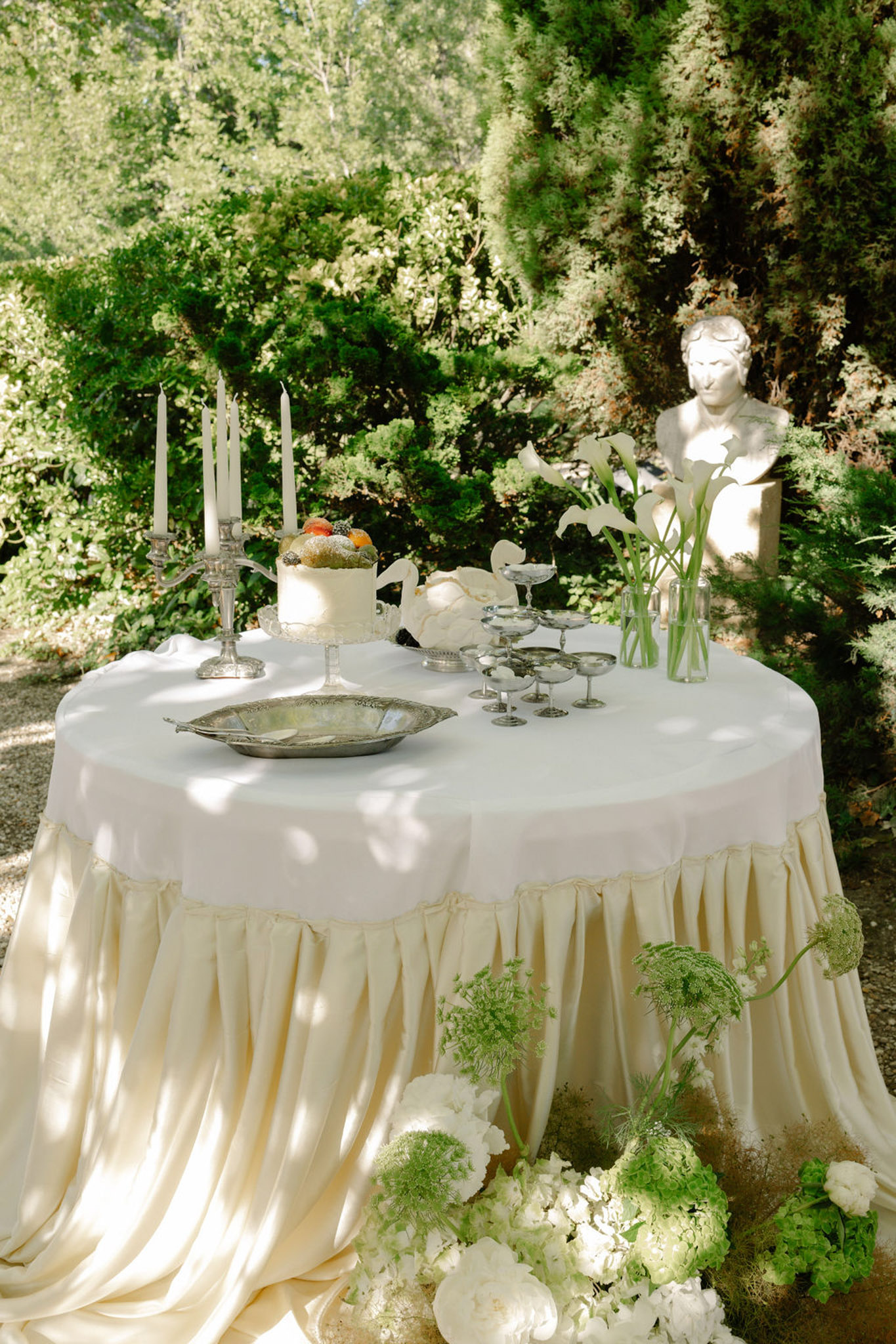 Round cocktail table with white linen, silver candelabra, and cream floral arrangement