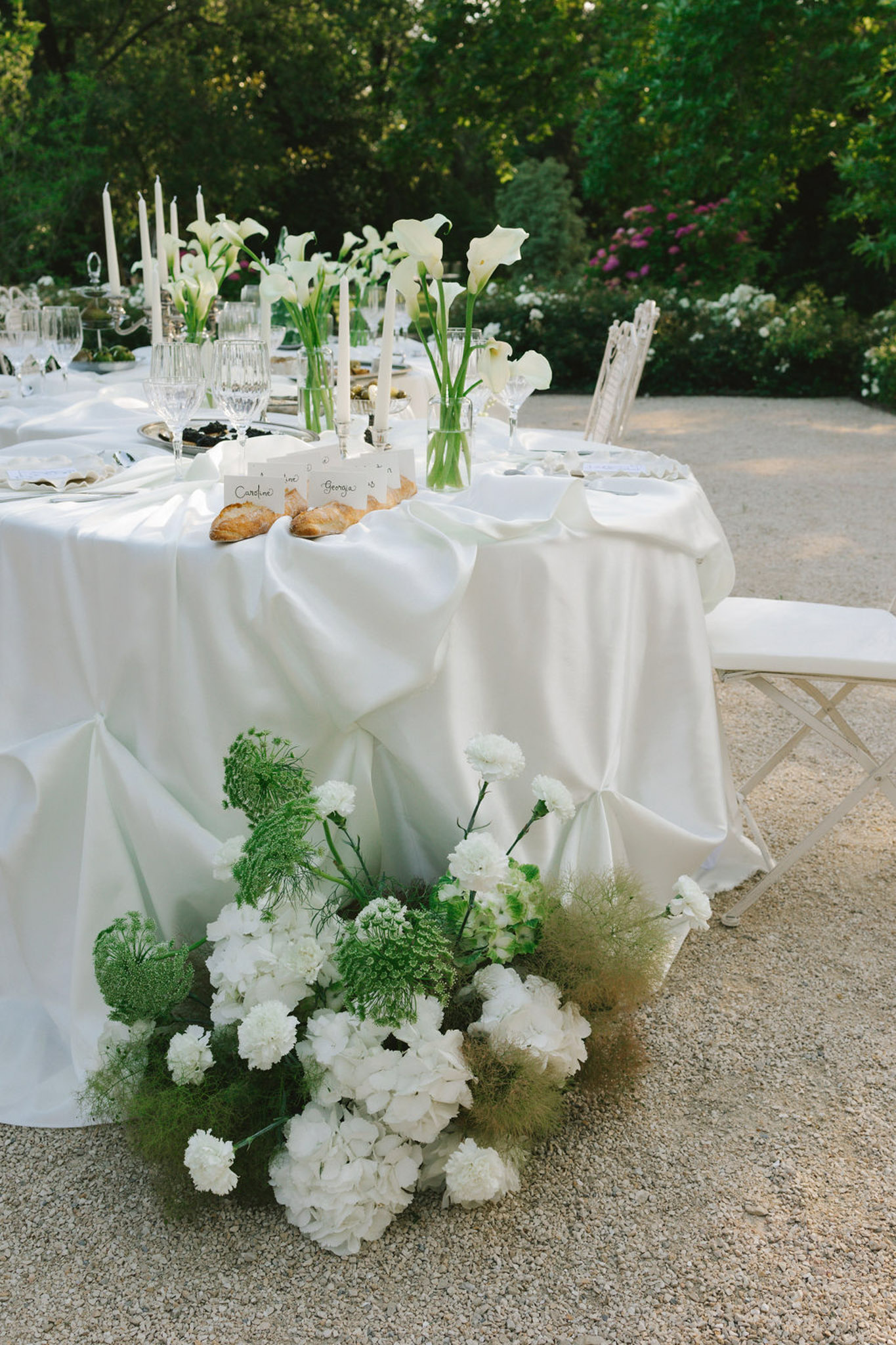 Outdoor reception tables with ivory linens, white calla lily centerpieces, floor arrangement of white carnations and grasses