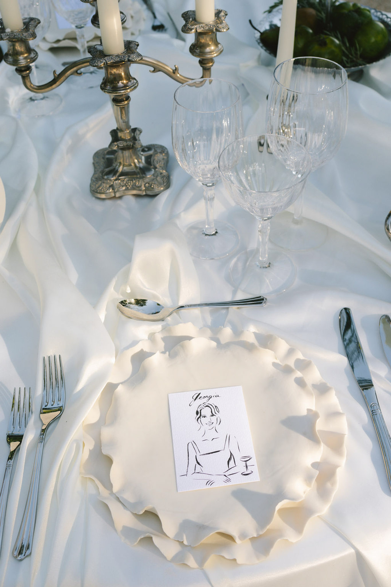 Formal place setting with ruffled charger plate, illustrated place card, and brass candelabra centerpiece