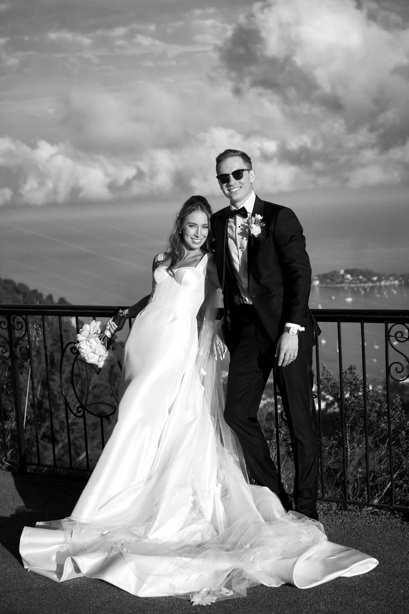 Black and white couple on terrace with mermaid gown train and coastal bay with boats behind