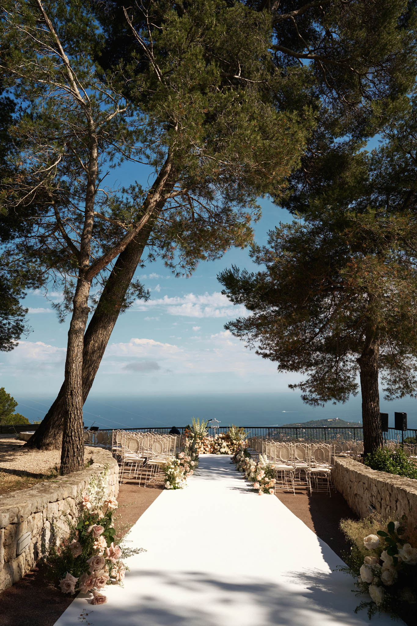 Outdoor ceremony aisle with white runner, gold chiavari chairs, and blush floral altar overlooking the sea