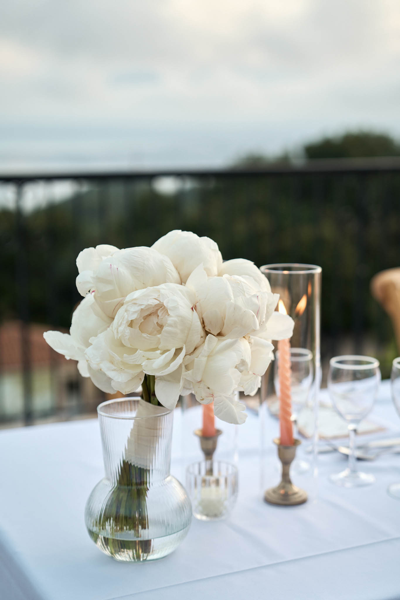 White peony centrepiece in ribbed glass vase with terracotta twisted tapers in brass candlesticks