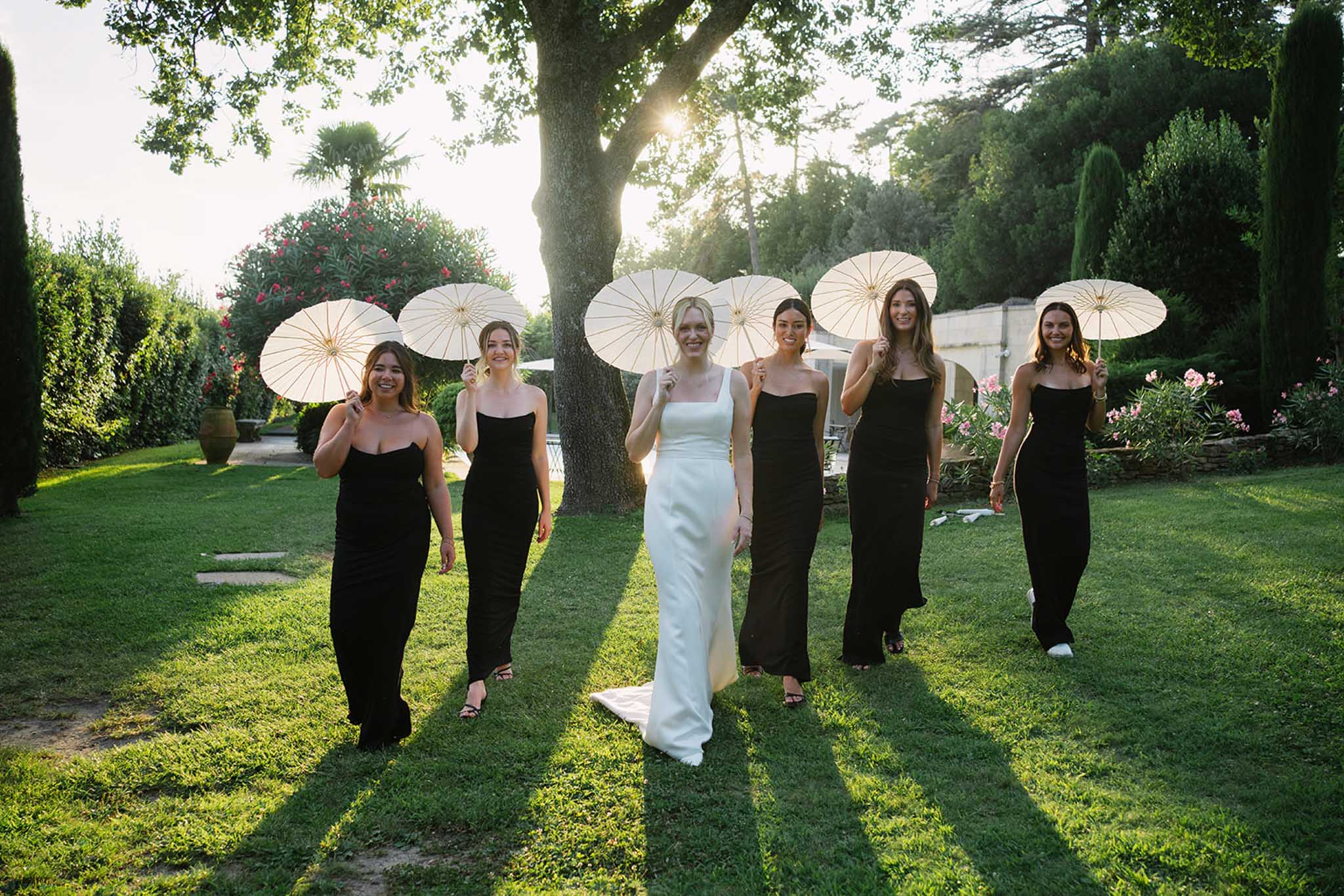 Bride with bridesmaid in black dress holding white umbrella outdoors at Château de Fontareches