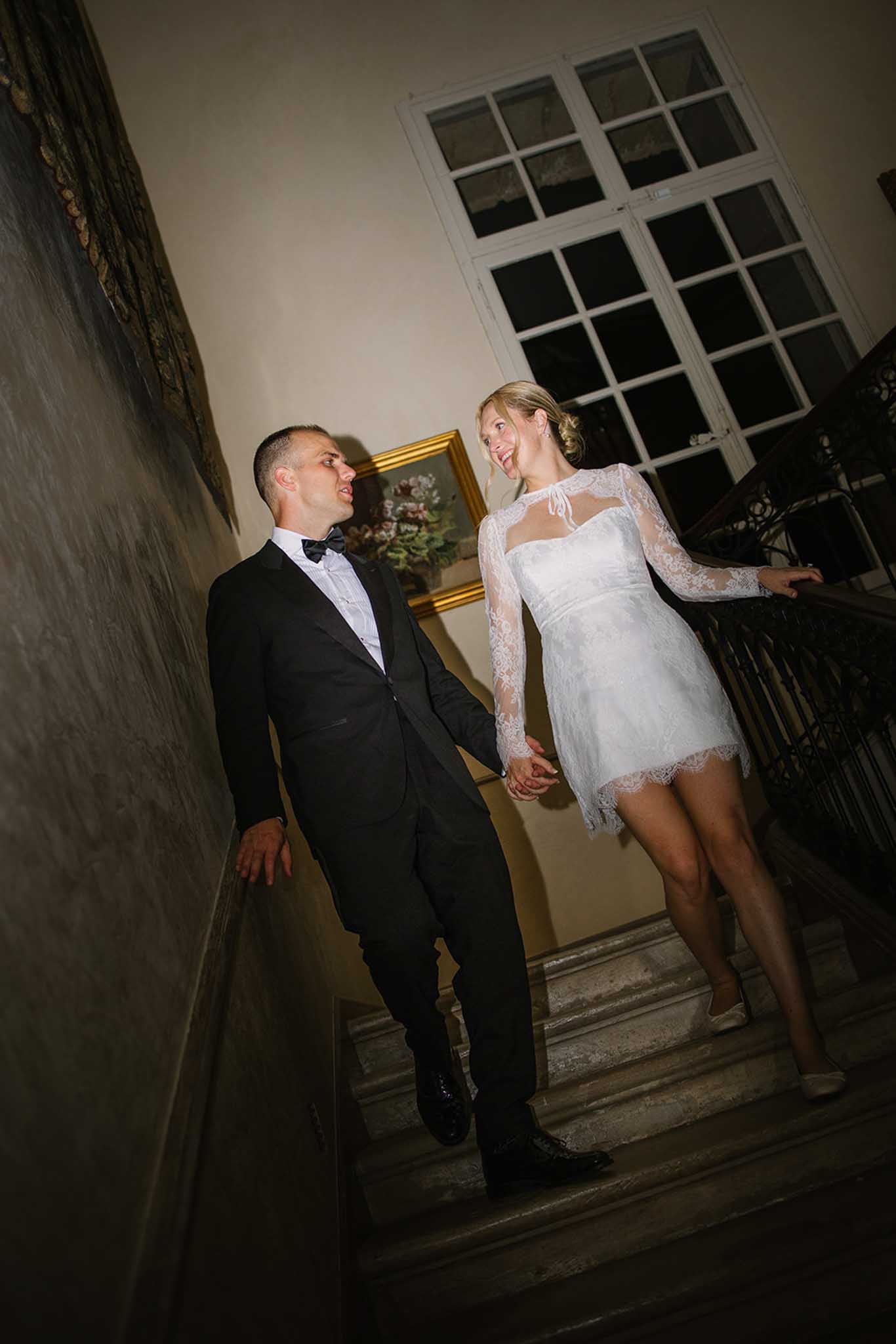 Bride in short white lace dress and groom descending staircase during evening reception