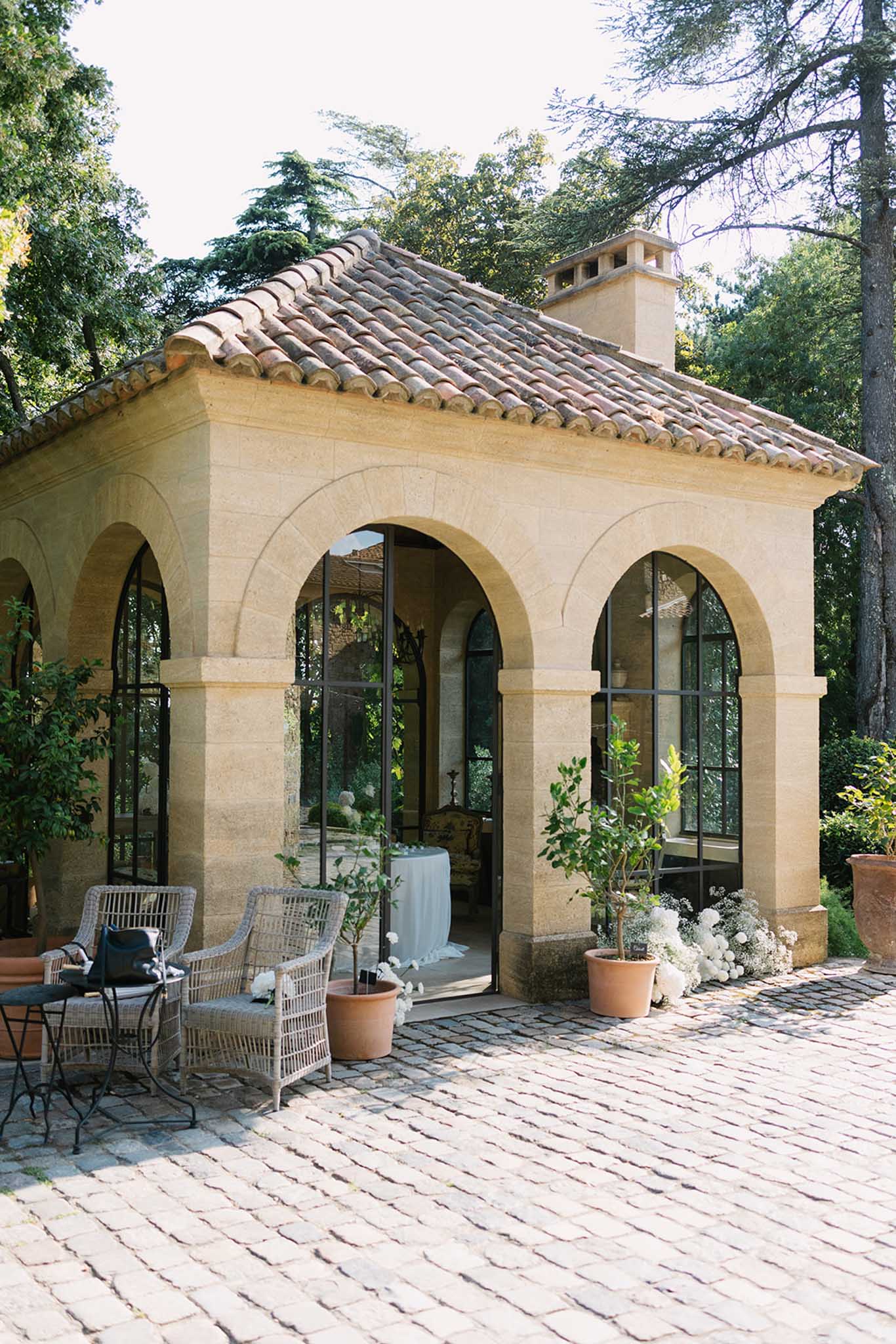 Mediterranean pavilion with arched doorways and terracotta roof set among mature trees in garden venue
