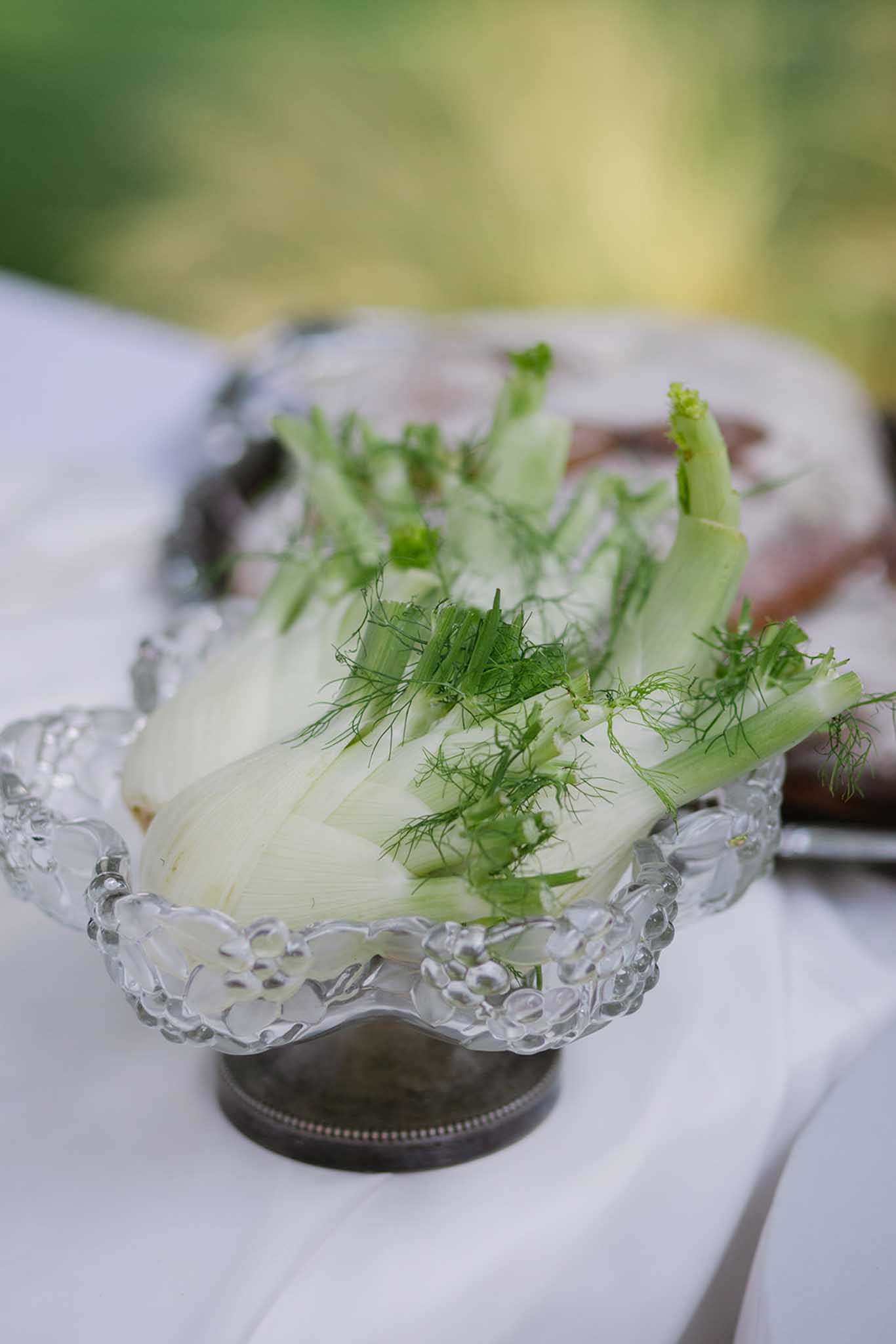 Fennel appetizer with dill in glass shell-shaped dish on white linen at outdoor reception