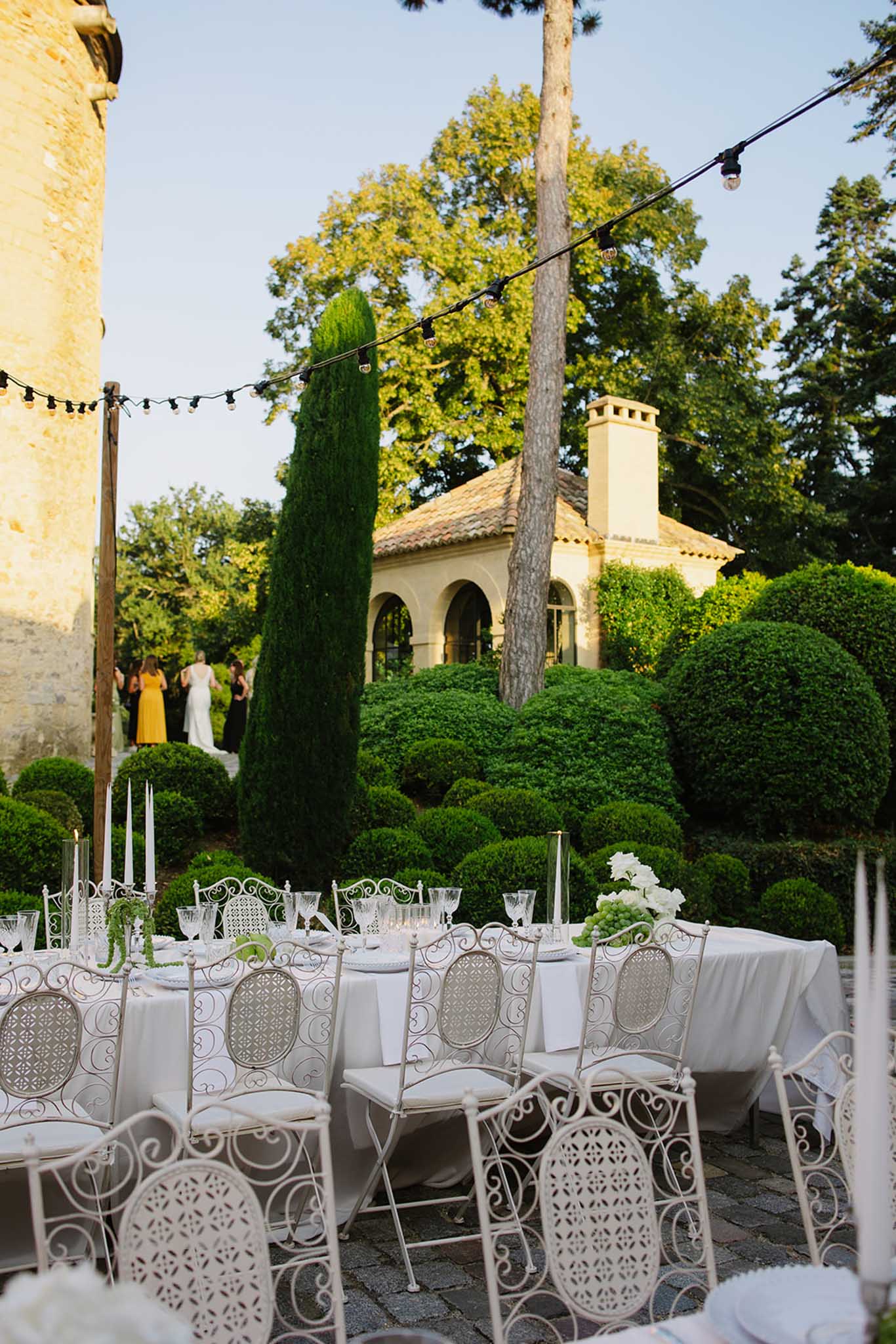 Outdoor reception terrace with wrought-iron chairs, white florals, and Mediterranean stone buildings