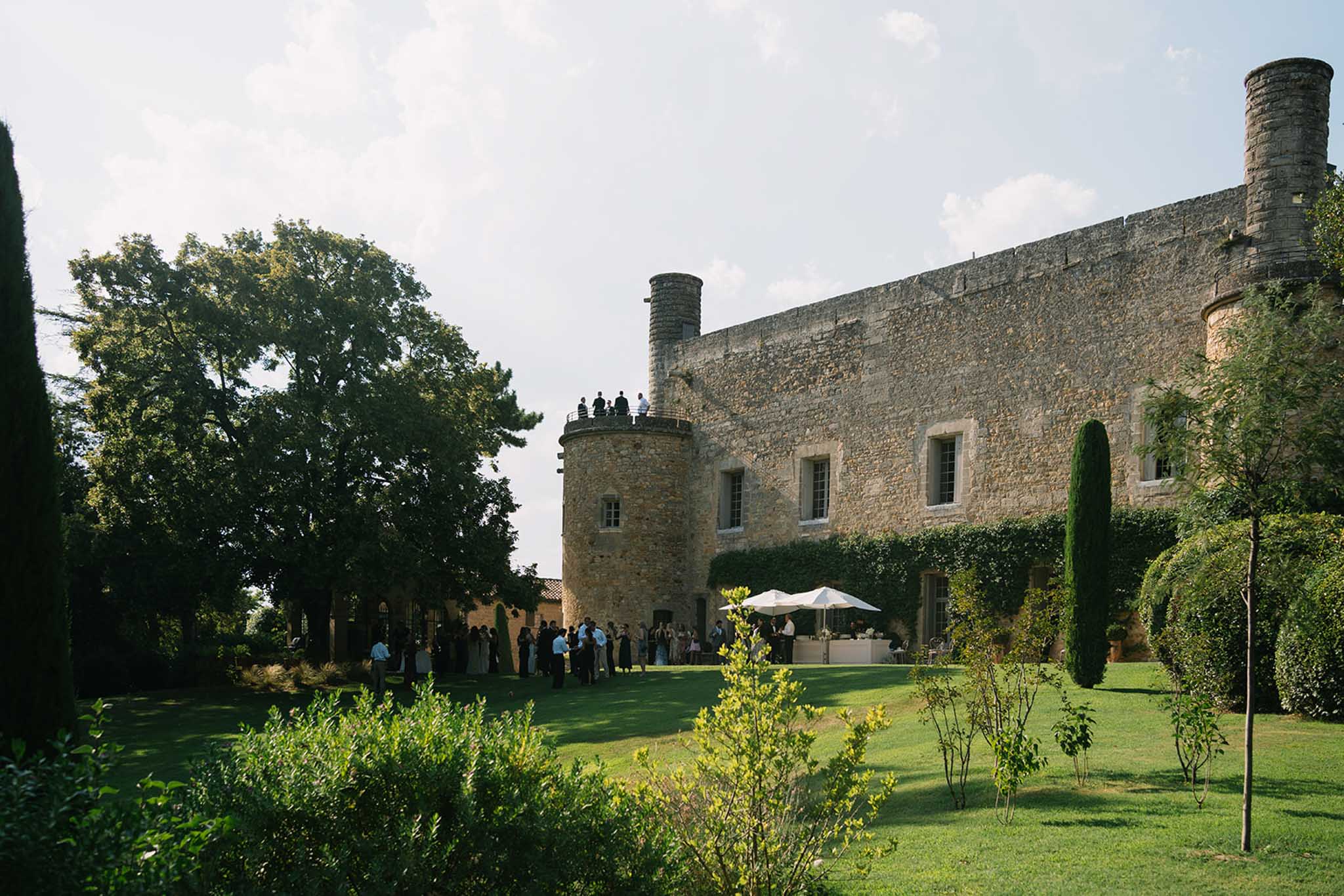 Medieval stone castle with round towers and crenellated walls surrounded by cypress trees and manicured lawn during reception