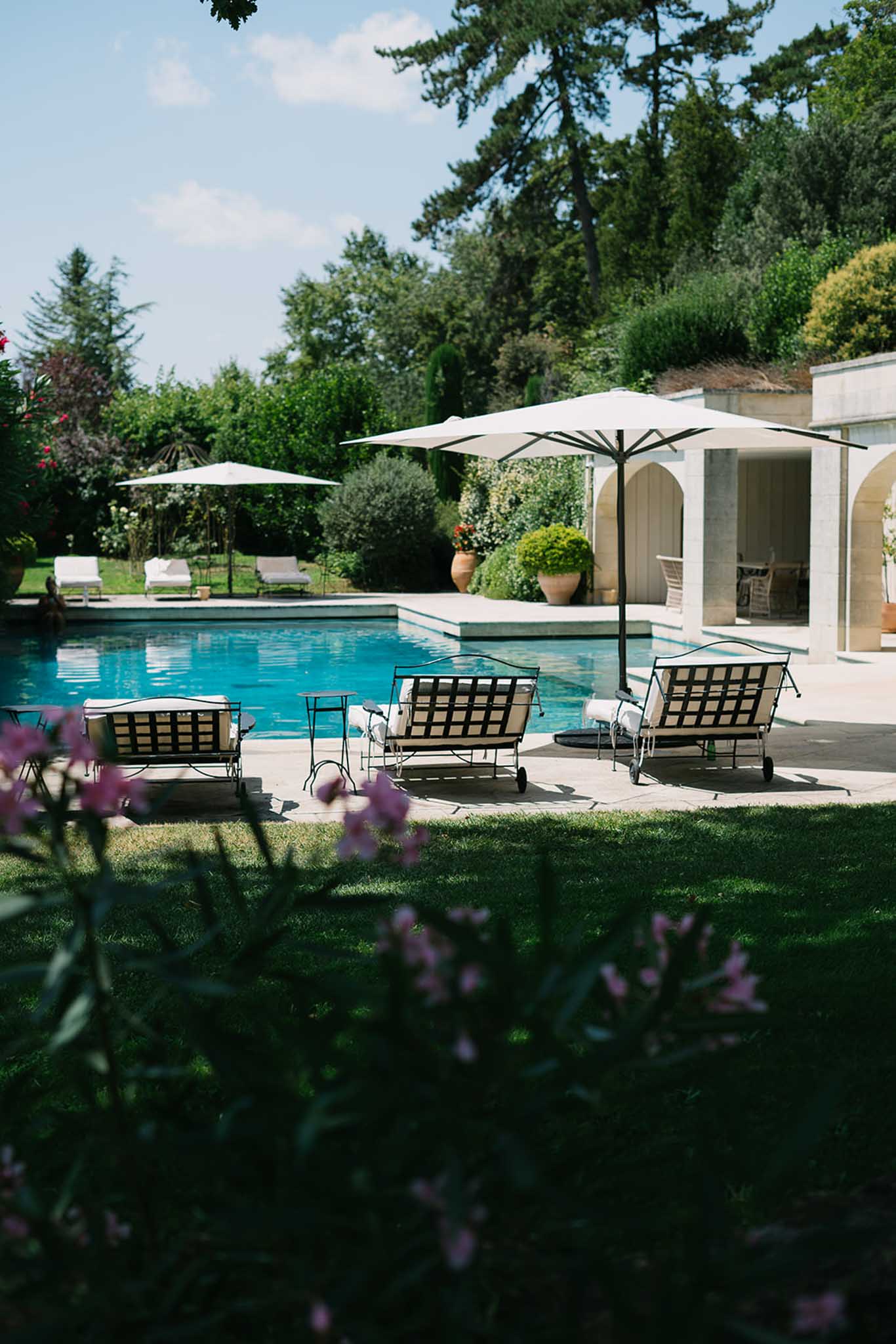 Luxury pool with white pavilion, black lounge chairs, and terracotta planters at outdoor wedding venue