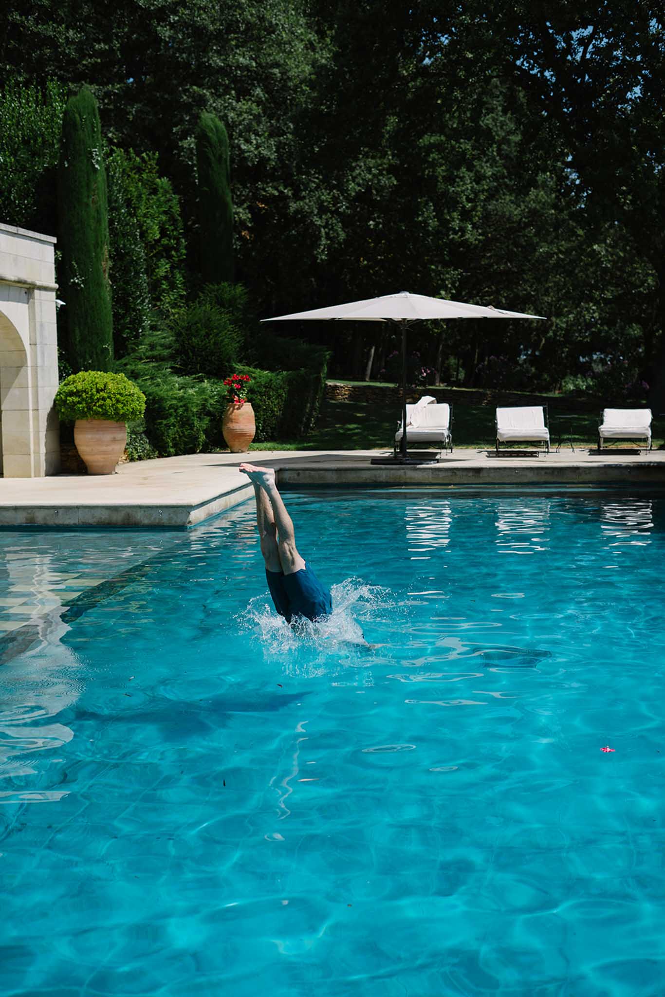 Guest diving into turquoise pool at venue with white loungers, cypress trees, and cream pool house