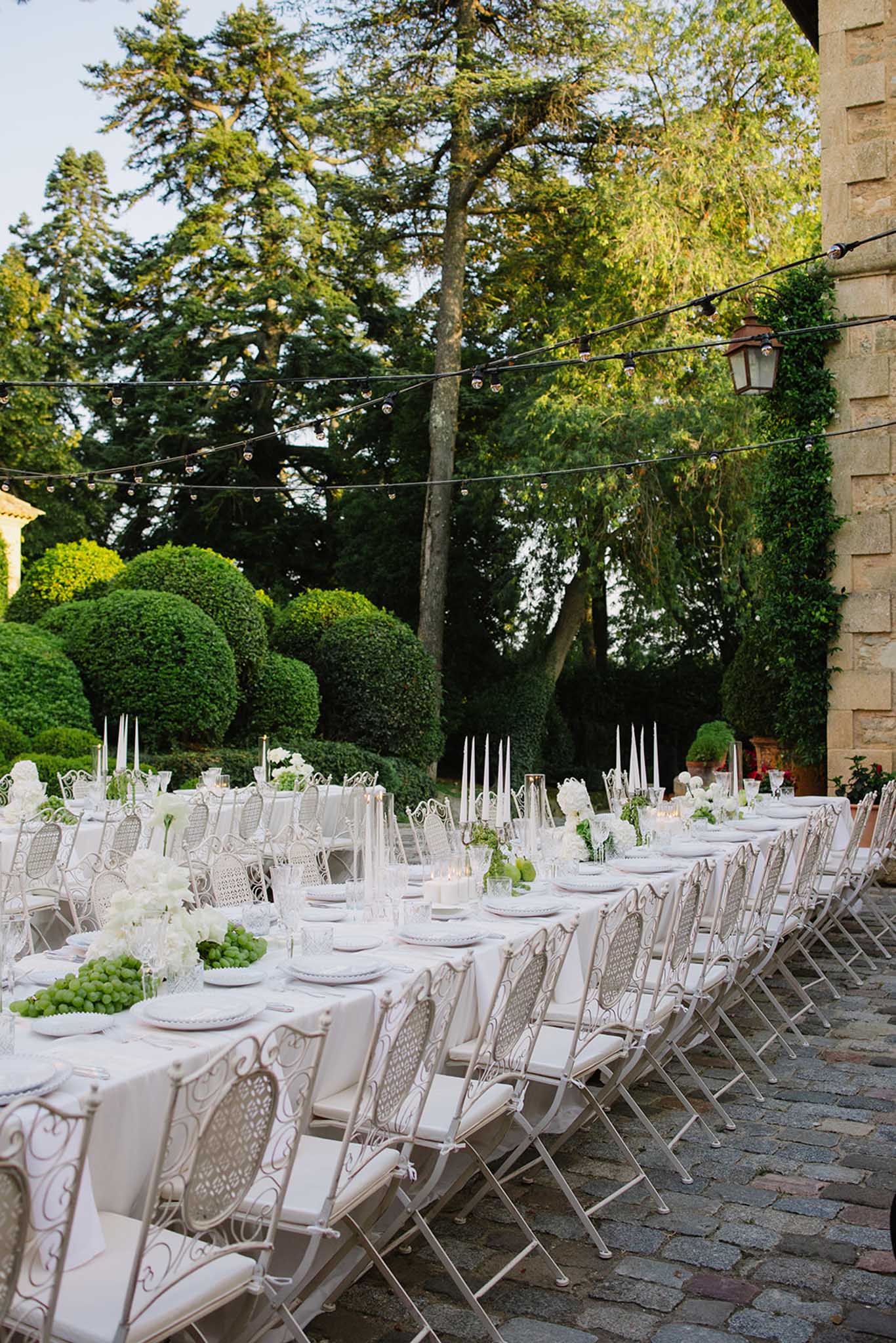 Long reception tables with white linens and ornate chairs in outdoor courtyard