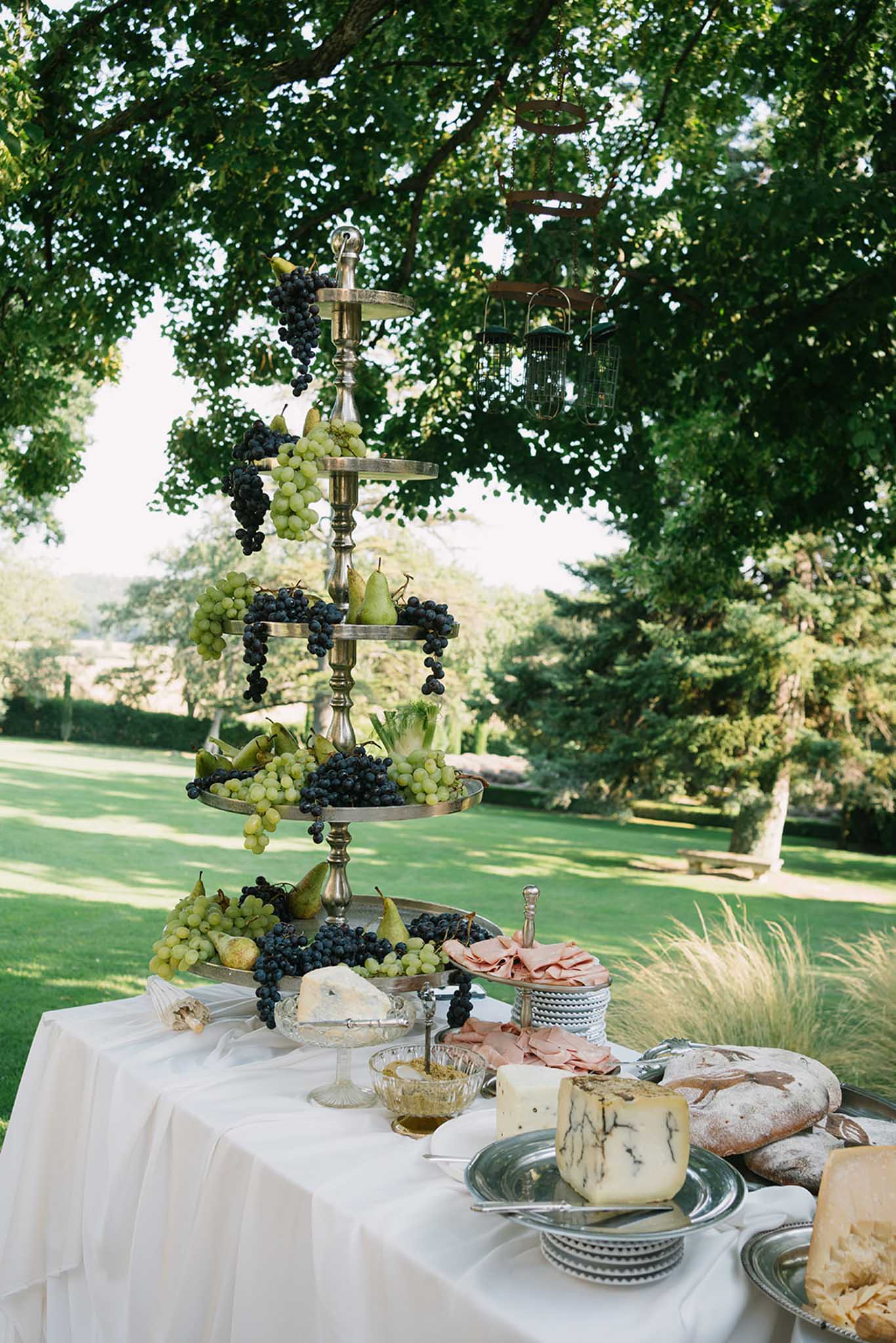 Tiered brass stand with grapes, cheese, and artisanal breads on outdoor reception table
