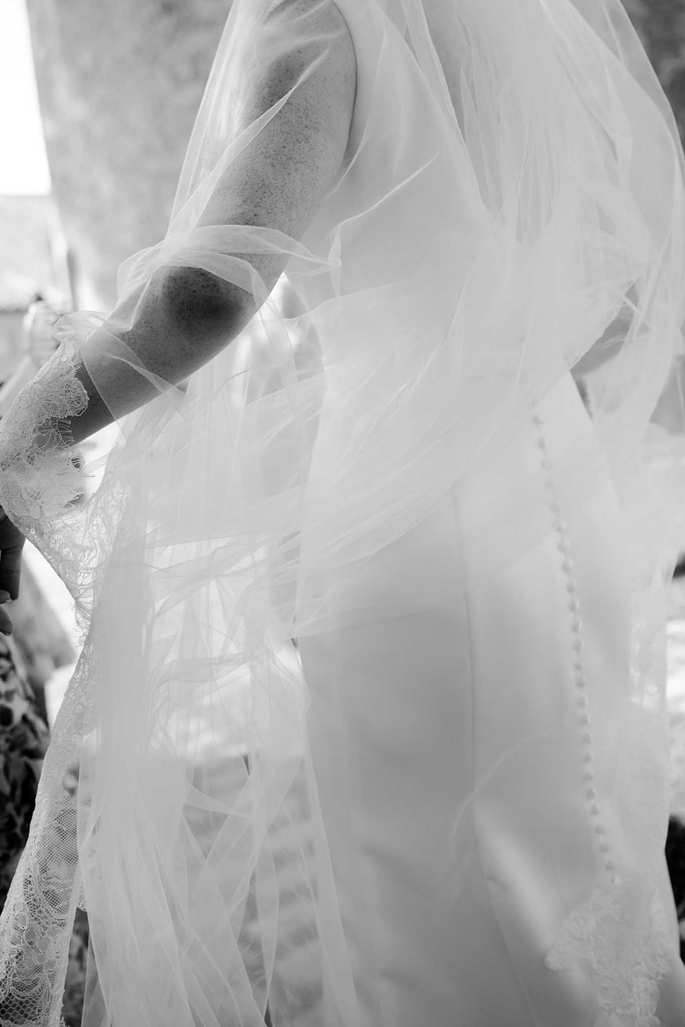 Black and white close-up of bride's arm and shoulder showing layered tulle and intricate lace detailing on bridal gown