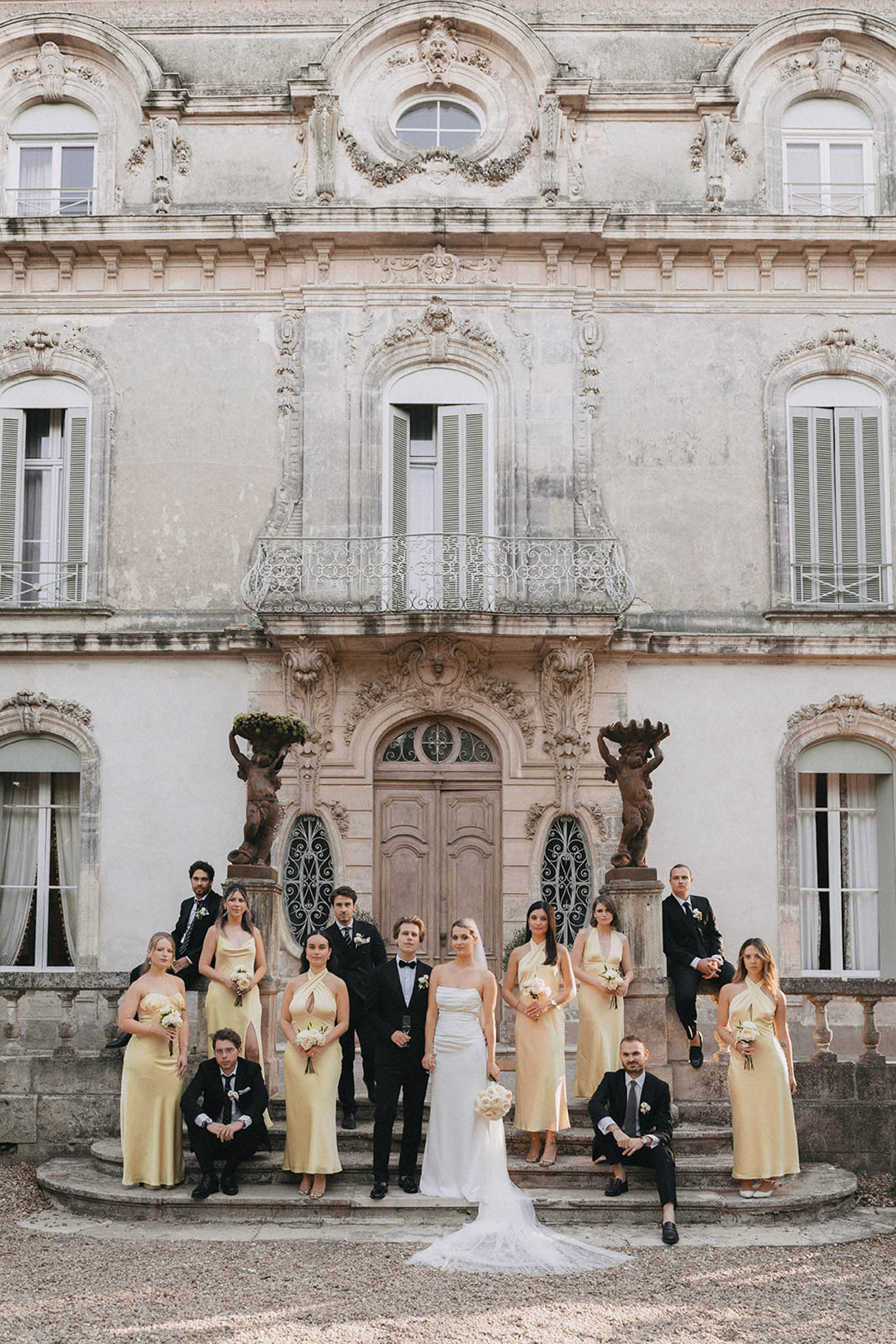 Formal bridal party portrait on chateau steps with bridesmaids in champagne dresses and groomsmen in black suits