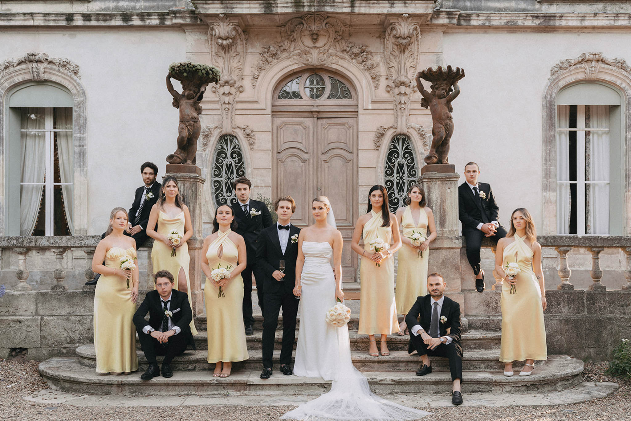 Full wedding party portrait on neoclassical building steps, bride in strapless gown, bridesmaids in pale yellow dresses
