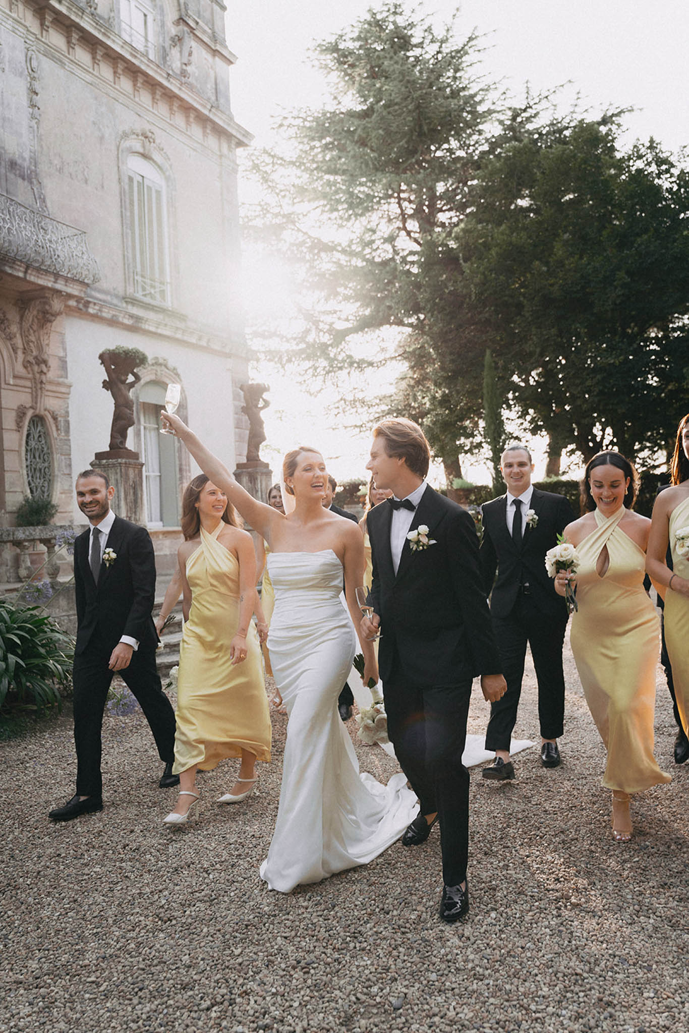 Bride and groom leading bridal party procession through estate courtyard with bridesmaids in yellow
