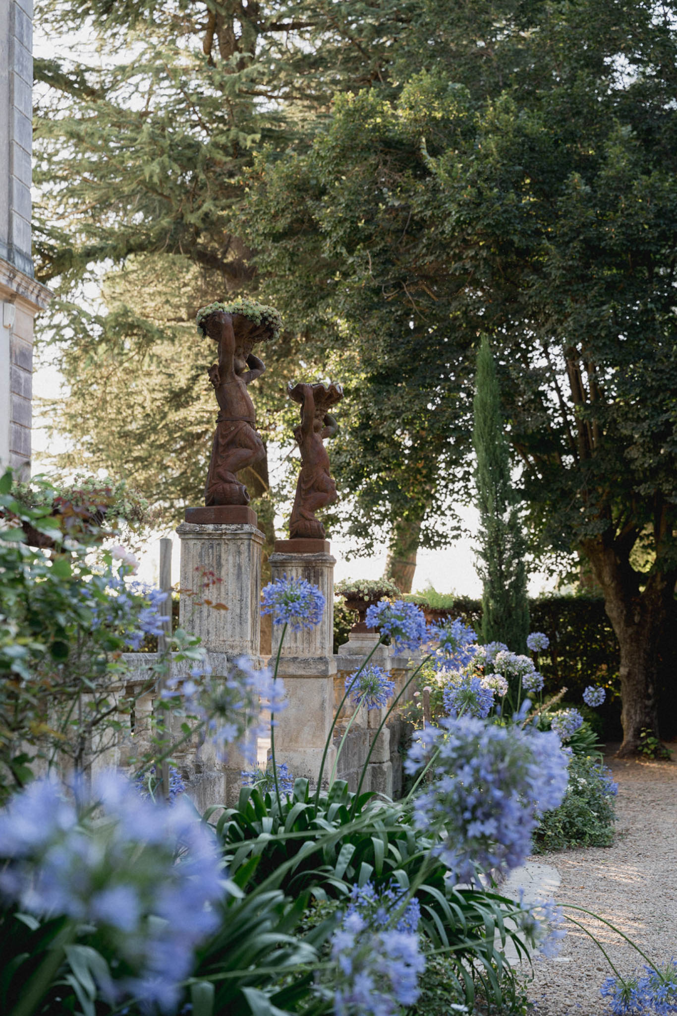 French formal garden with carved wooden finials on stone pedestals flanked by blue agapanthus flowers and cypress trees