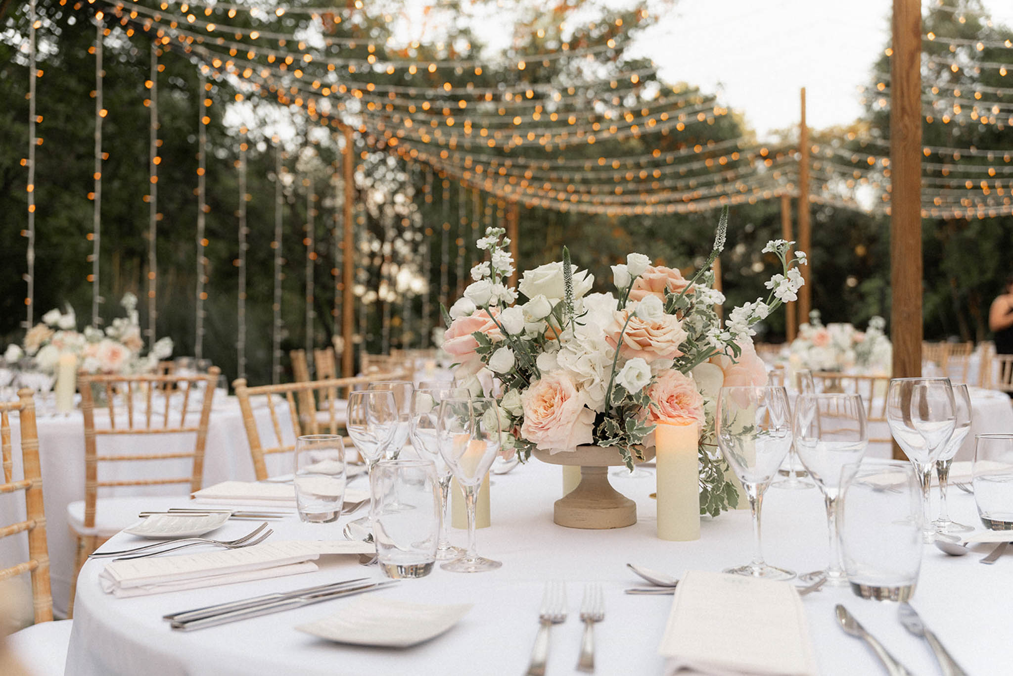 Outdoor reception under wooden pergola with golden lanterns and peach rose centerpieces