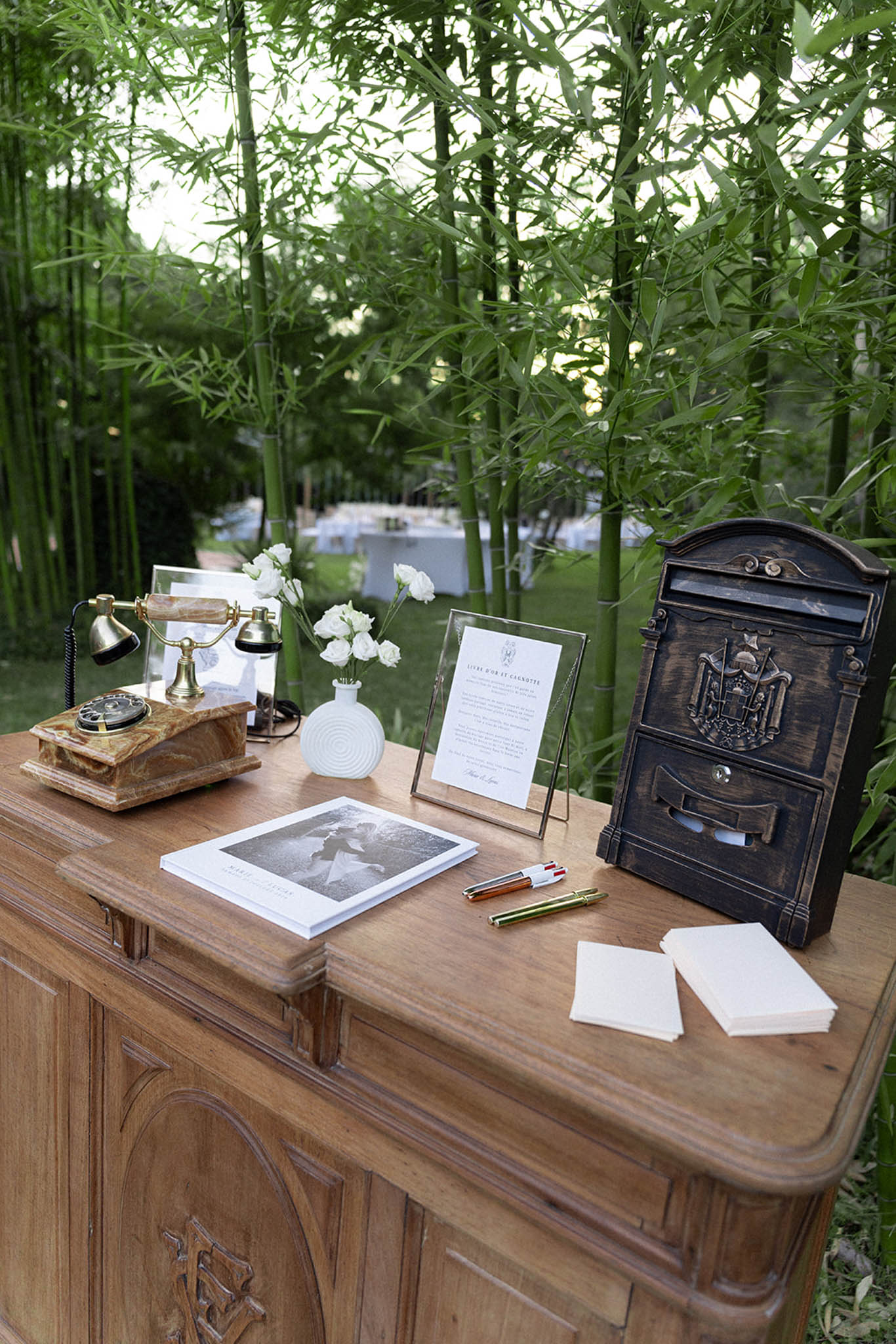 Vintage guest book table with brass rotary telephone, white flowers, and decorative mailbox in garden