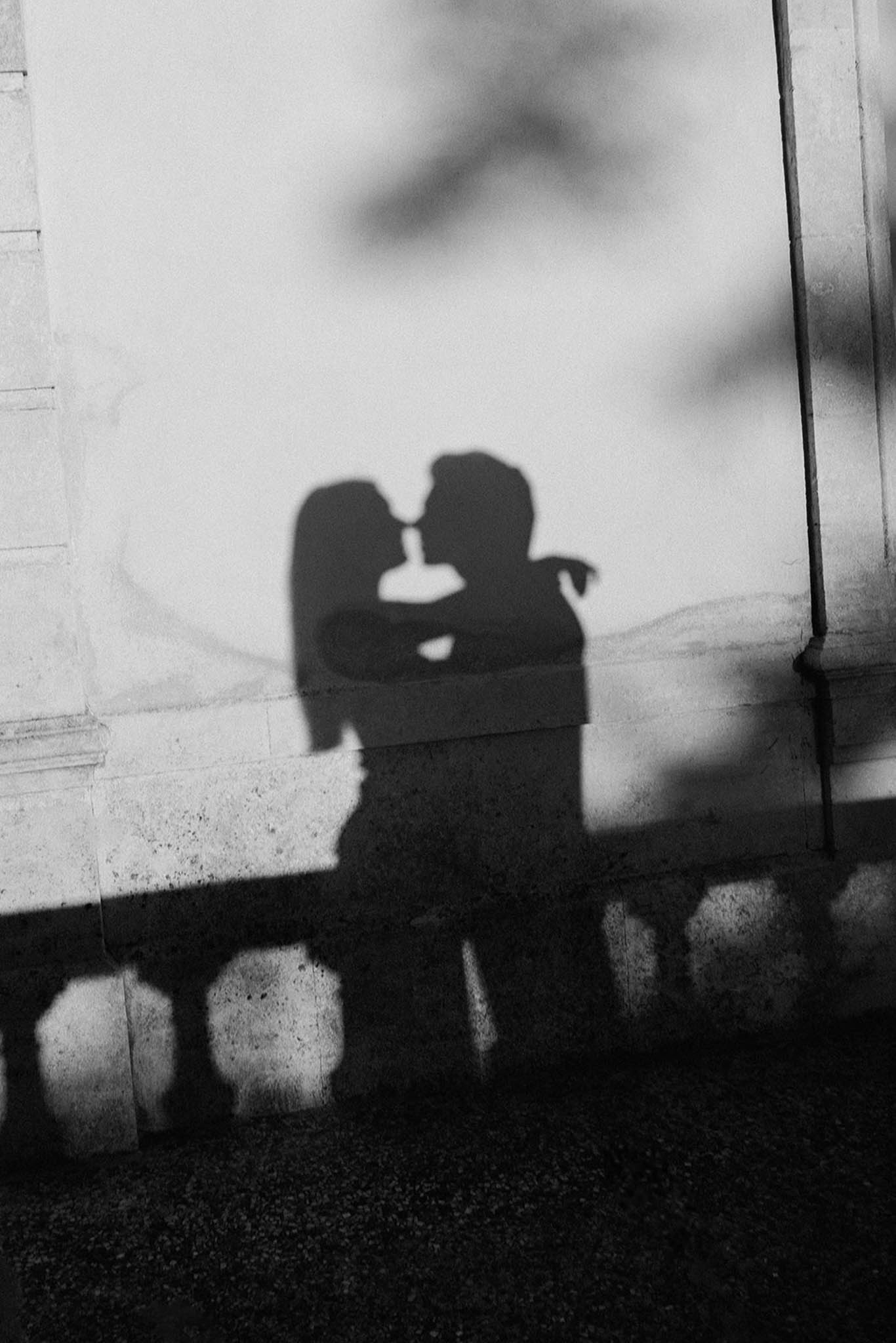 Black-and-white shadow silhouette of couple kissing projected onto light stone wall