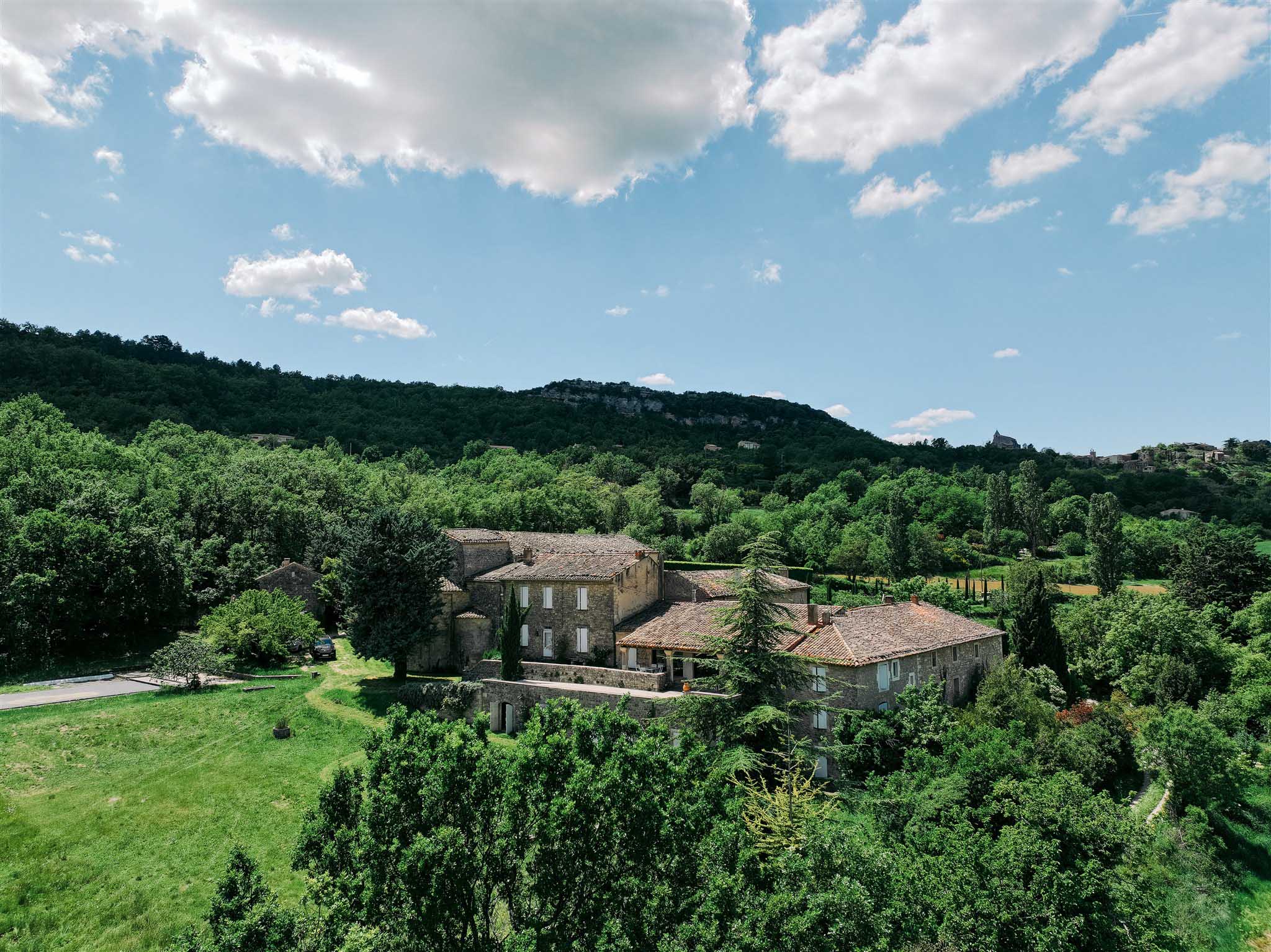 Aerial wide shot of stone estate with terracotta roofs surrounded by cypress trees and rolling countryside