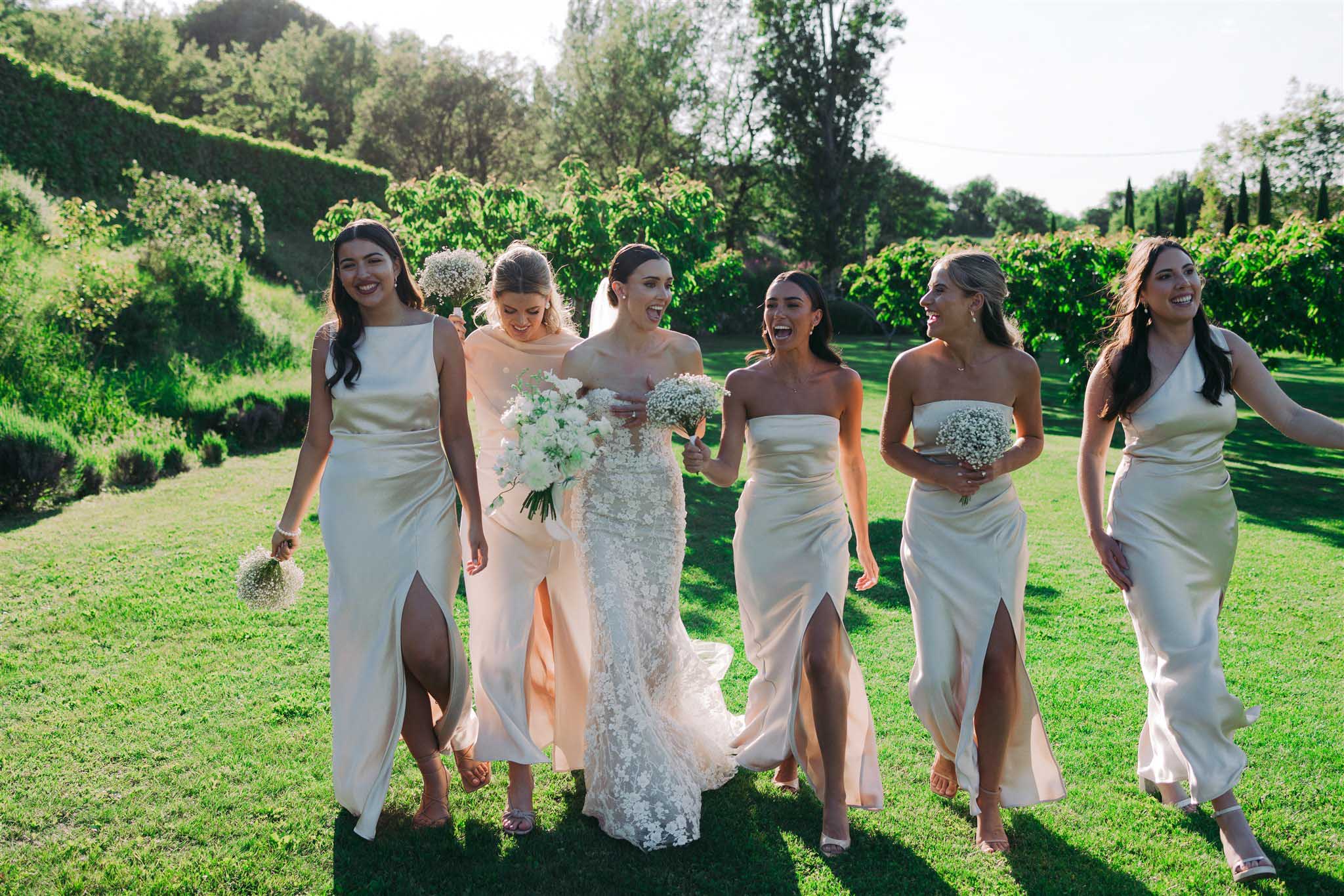 Bride in beaded ivory lace gown and six bridesmaids in pale champagne dresses walking across manicured lawn