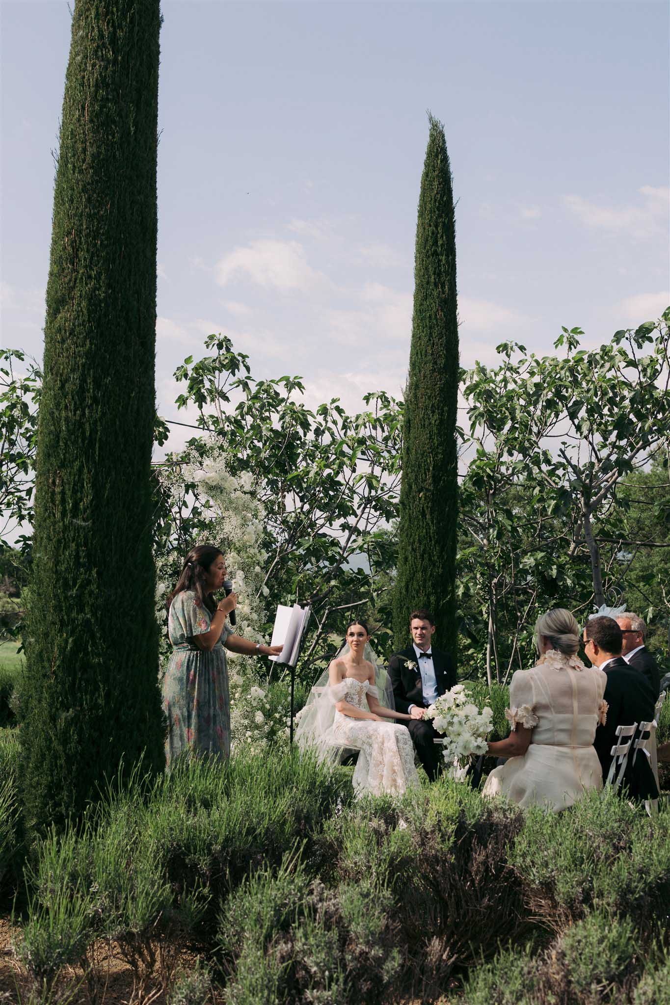 Bride and groom seated with celebrant at outdoor garden ceremony at Abbaye Saint-Eusèbe