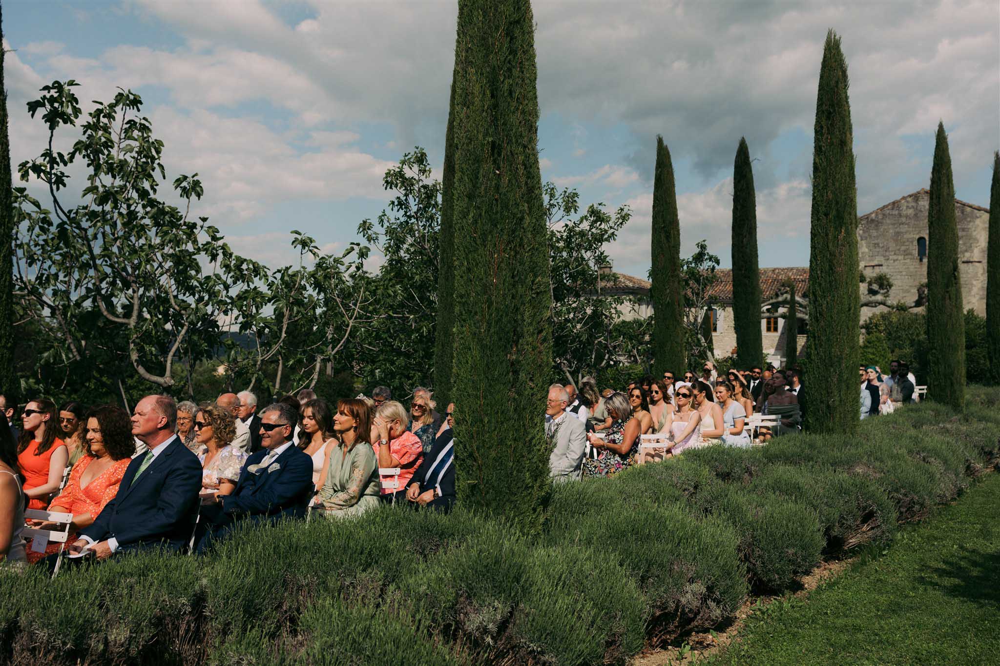Guests seated for outdoor ceremony at Abbaye Saint-Eusèbe surrounded by pine trees and wild plants