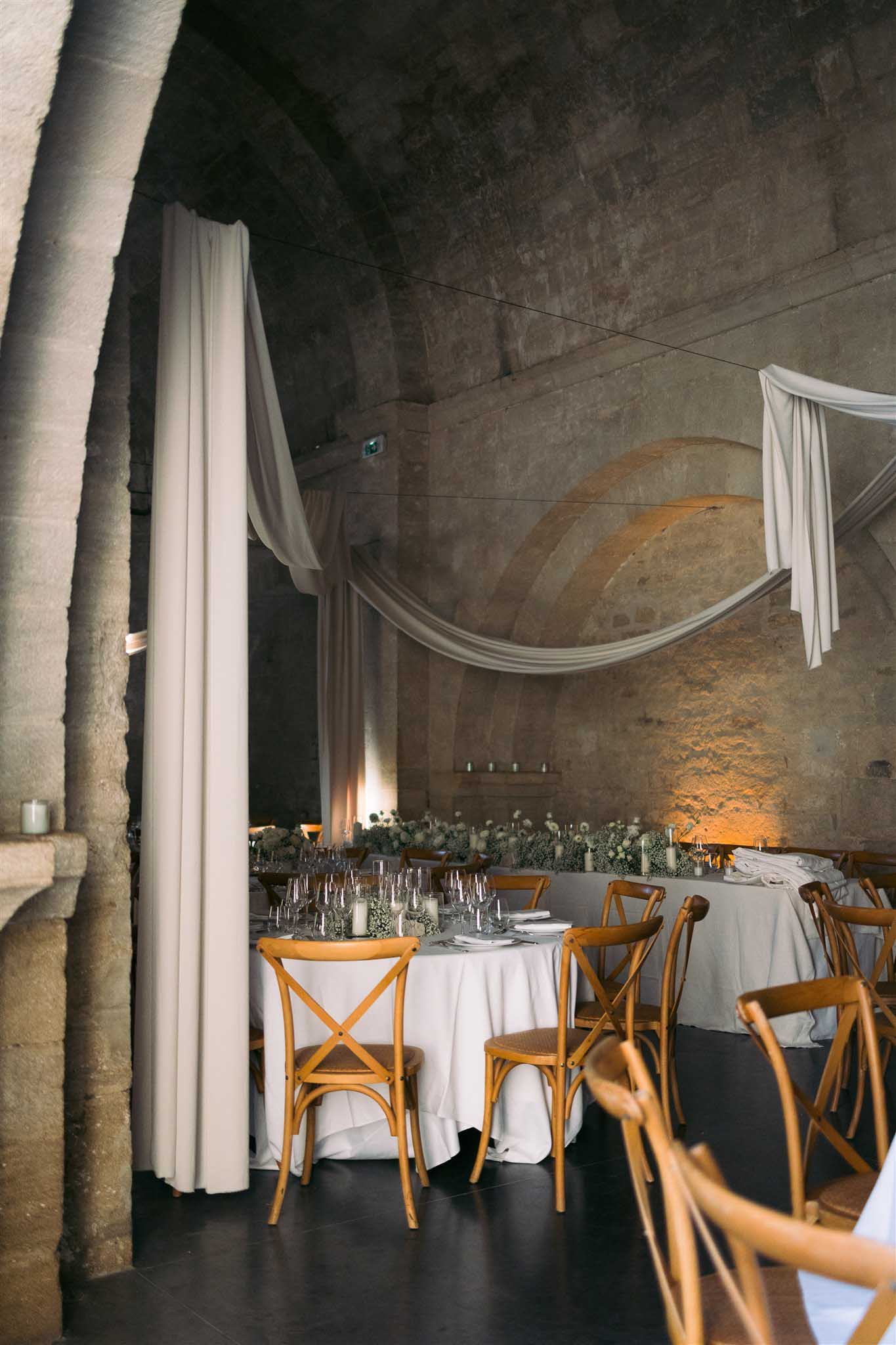 Reception tables with fabric draping inside historic stone vault with timber beams and uplighting