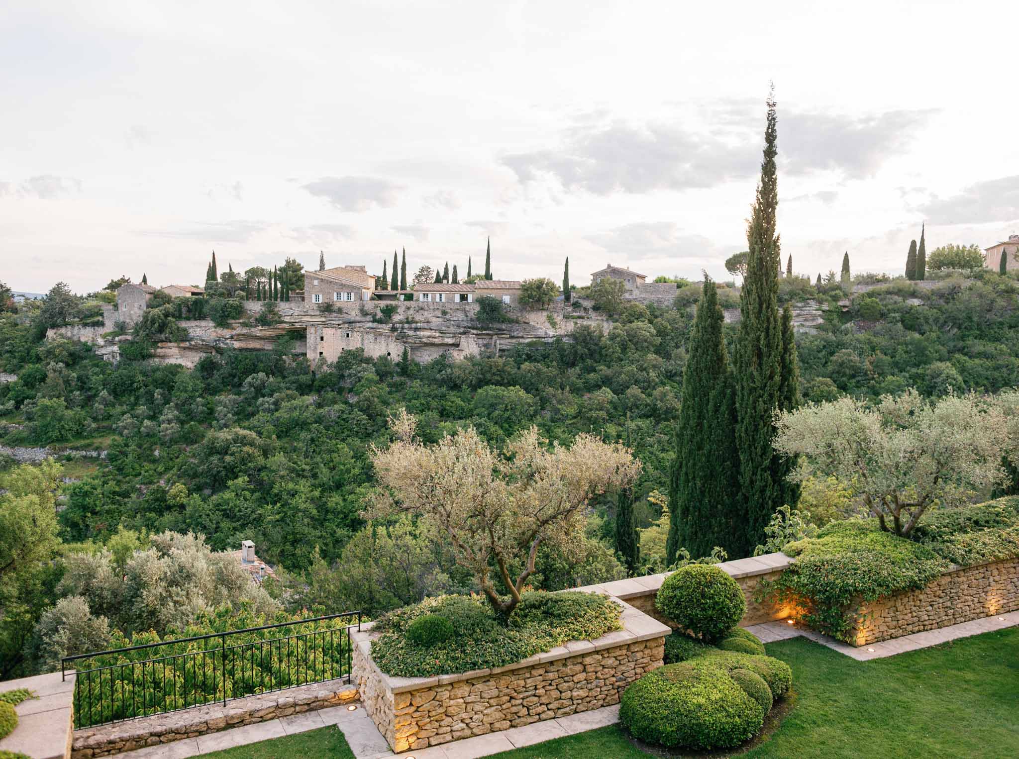 Stone terrace garden with boxwood hedges overlooking Tuscan hillside village and cypress-lined valley