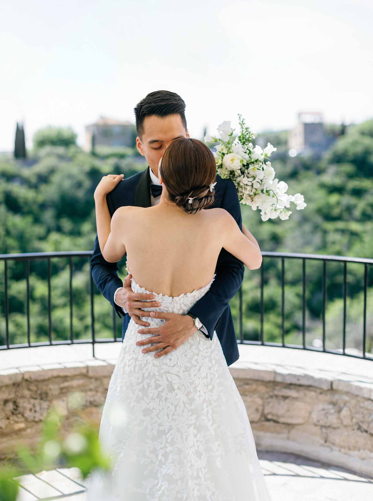 Bride and groom embracing on elevated terrace overlooking green Provencal hills and cypress trees