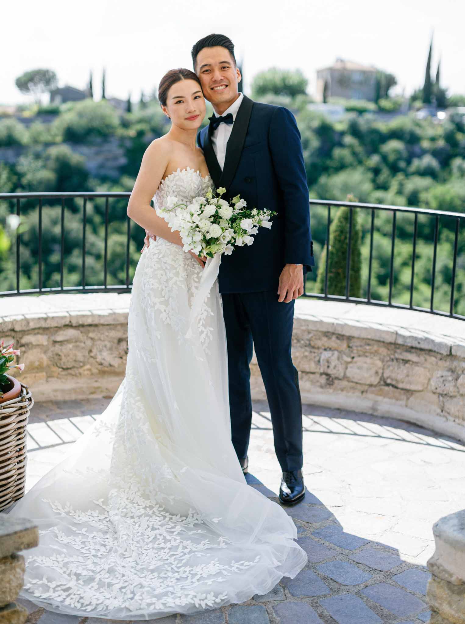 Bride and groom pose on stone terrace overlooking rolling hills with cypress trees at wedding venue