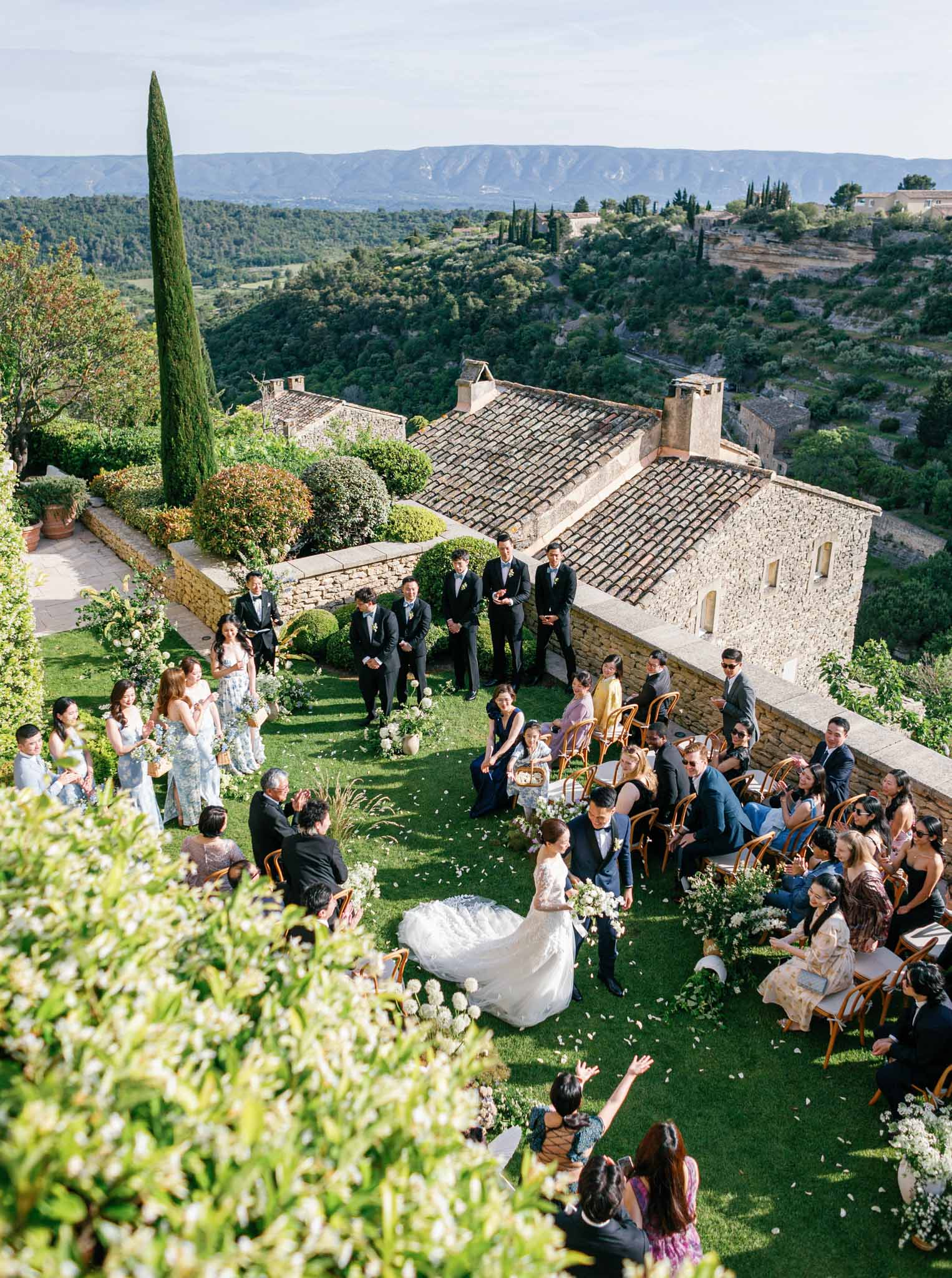 Aerial view of outdoor ceremony on lawn beside Provencal stone villa with terraced vineyards beyond