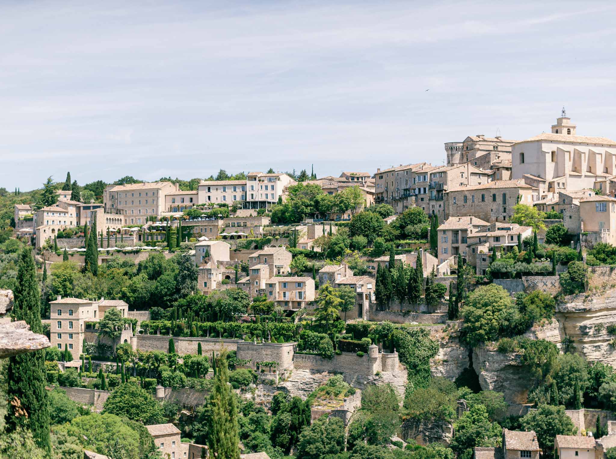 Medieval hilltop village in Provence with terracotta stone buildings, bell tower, cypress trees and river below