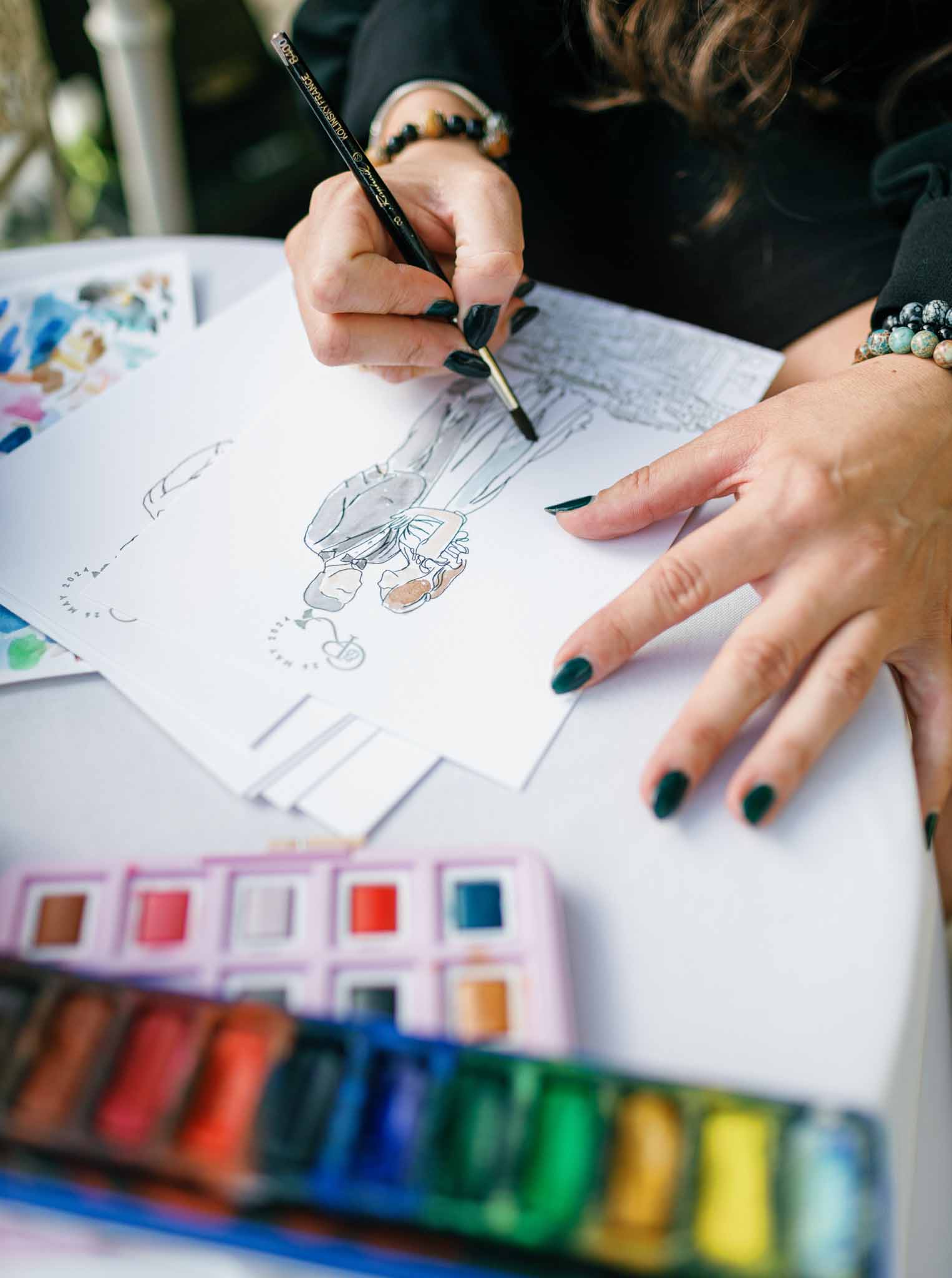 Guest with dark green nails sketching illustration at interactive art activity station with watercolor palettes