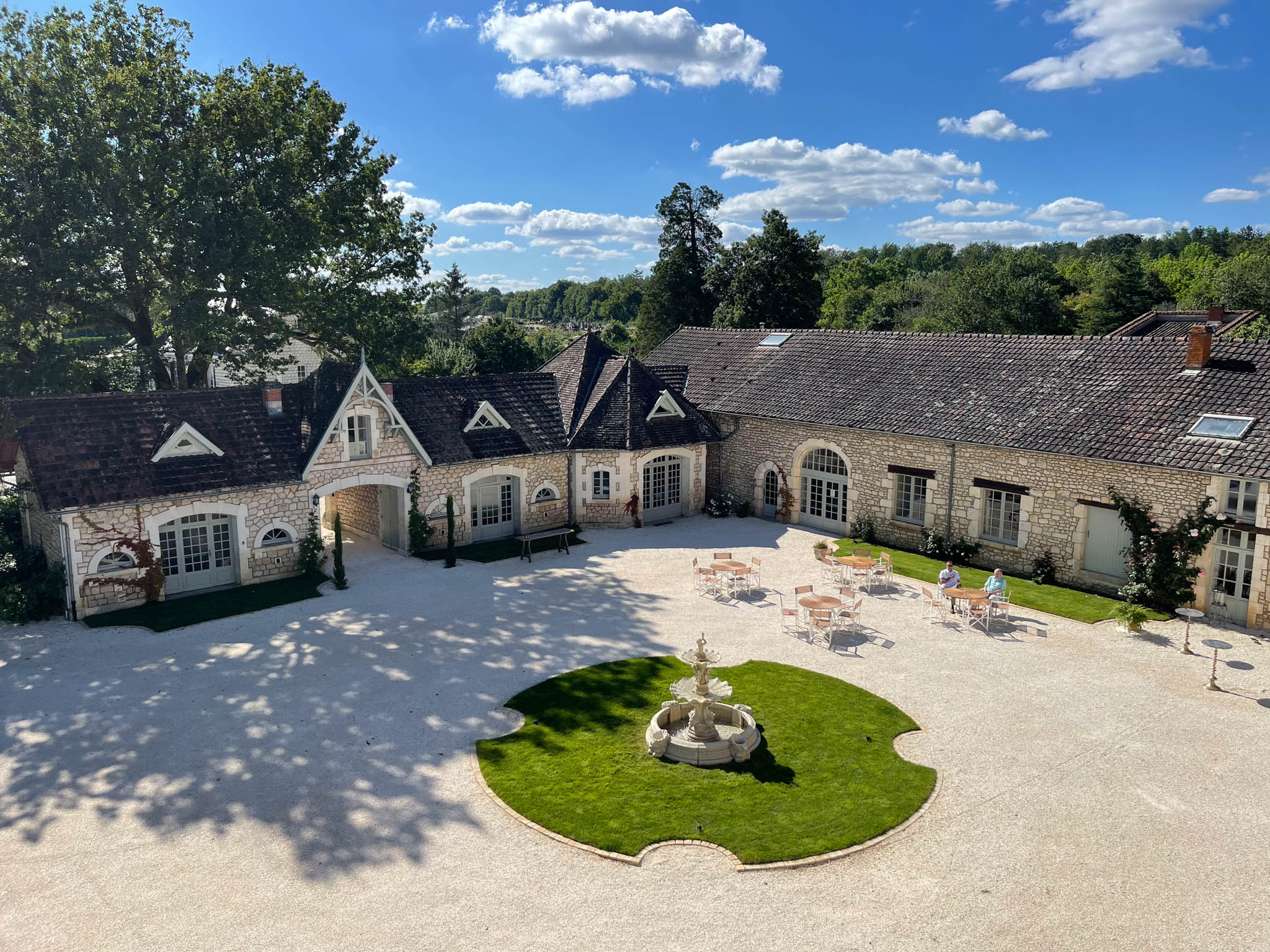 Aerial view of U-shaped French limestone estate with gravel courtyard, stone fountain, and topiary entrance