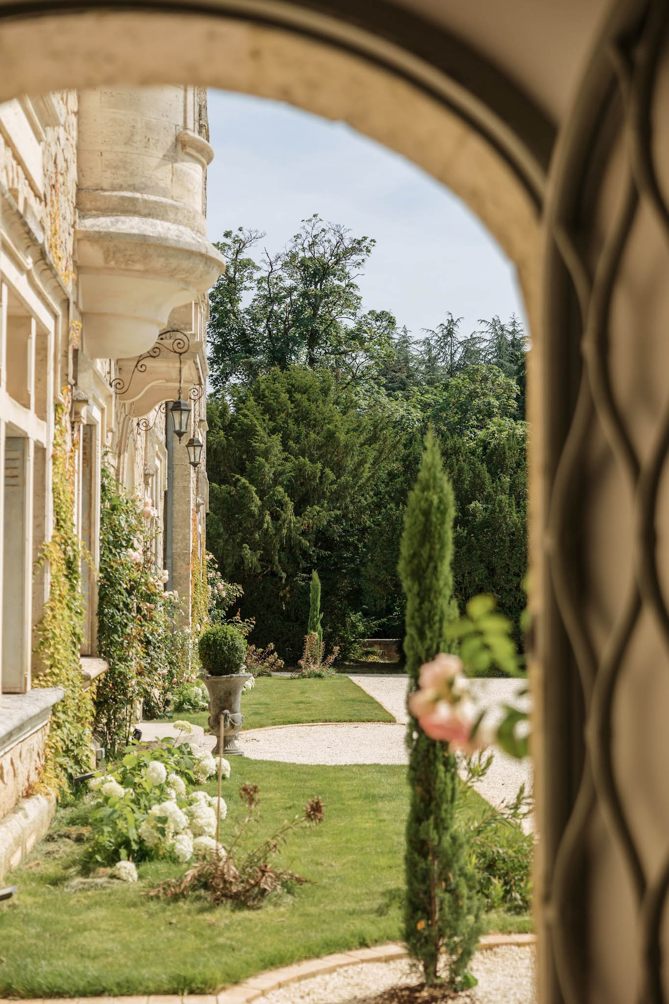 Chateau de la Couronne exterior viewed through arched doorway with formal garden, topiary, and hydrangeas
